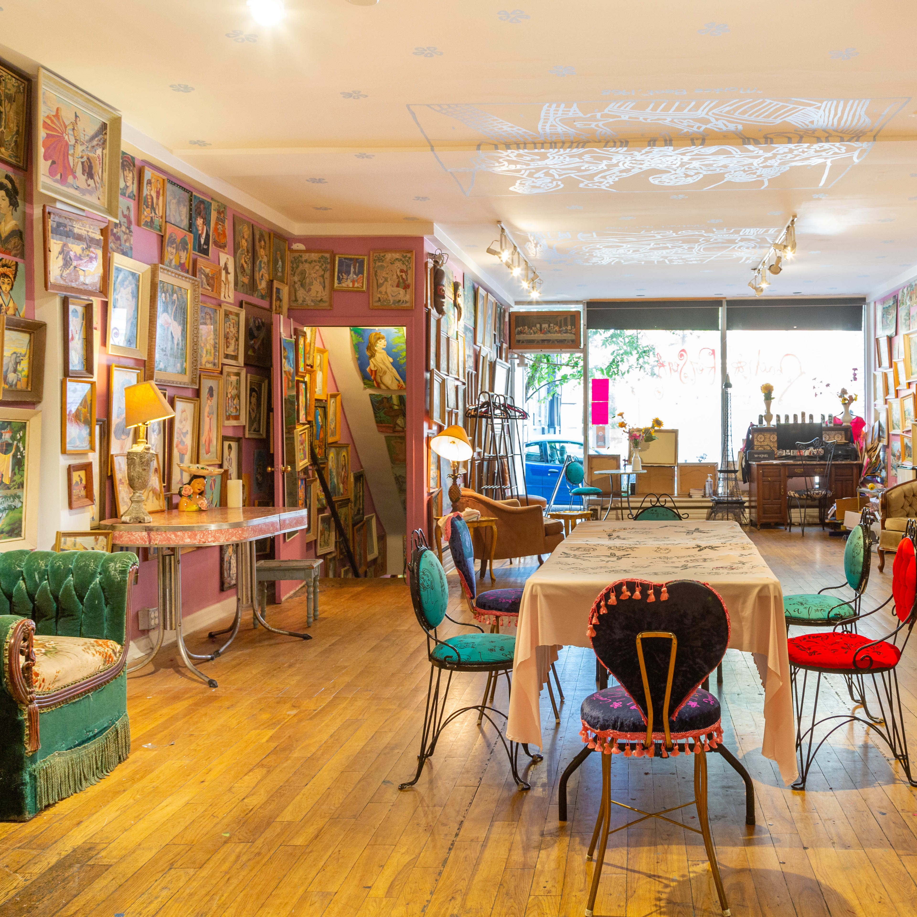 A colorful art-filled room with a long dining table in the center, surrounded by various chairs, and walls adorned with framed artworks.