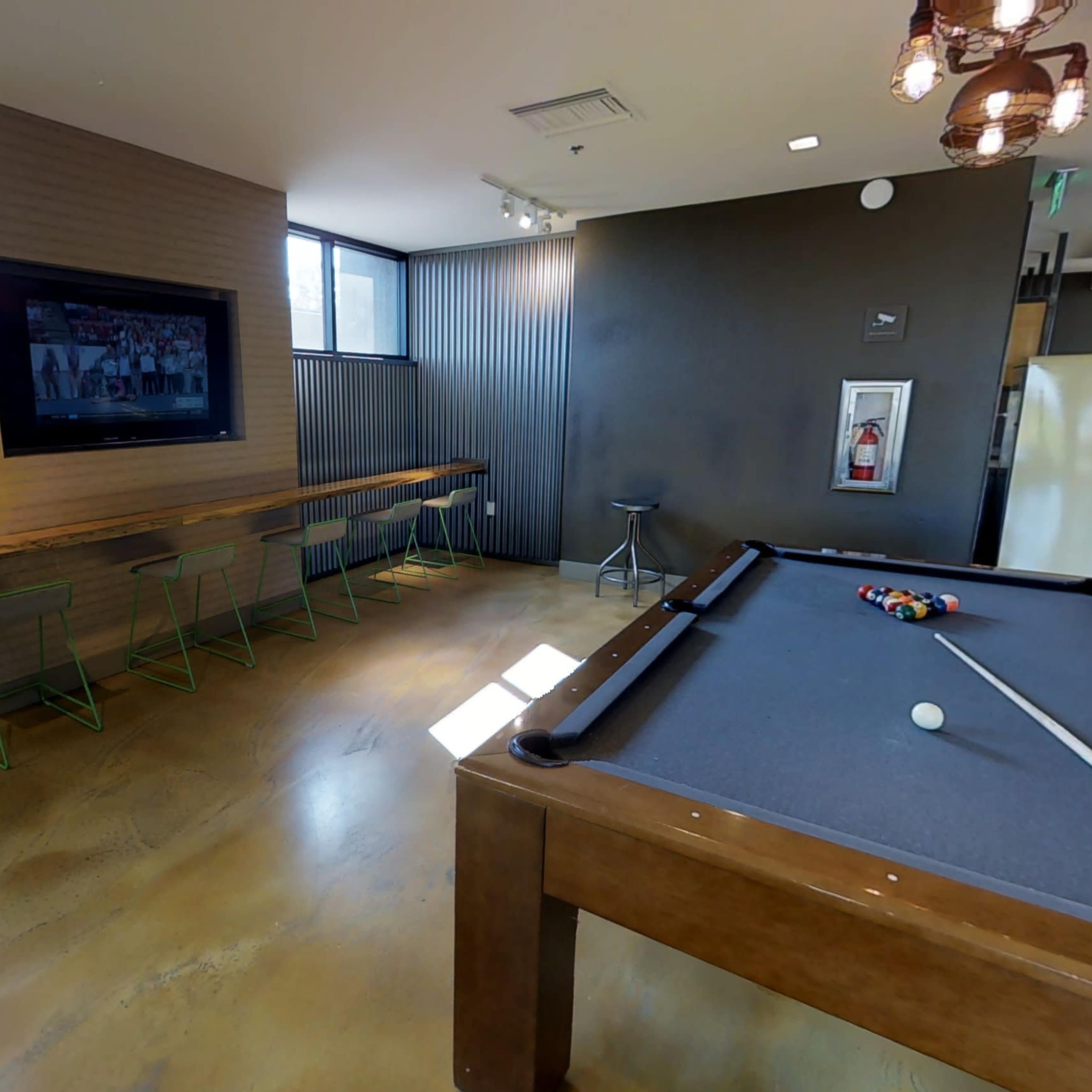A lounge area featuring a pool table, a bar-like seating space along the wall, and a television mounted on the opposite wall.