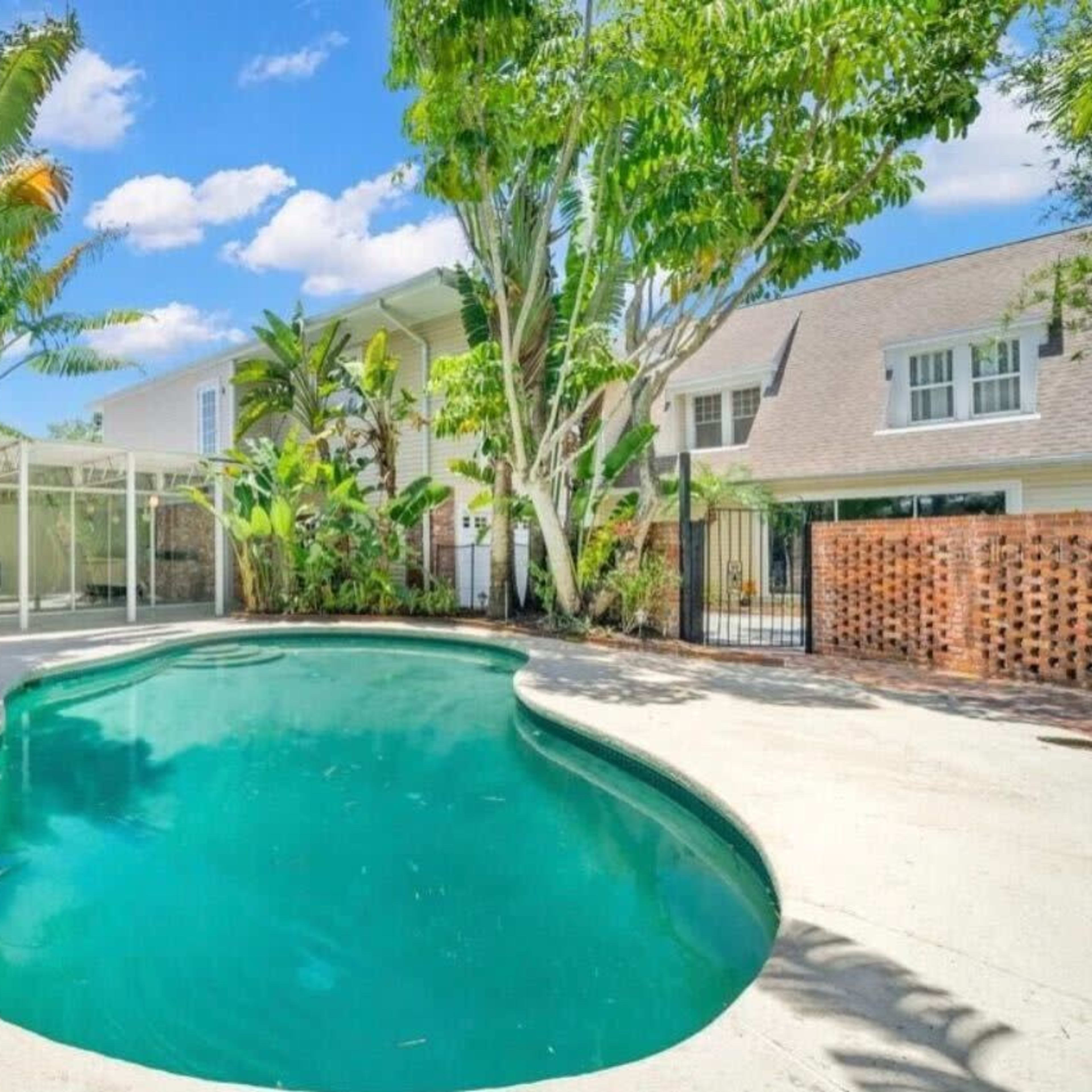 A swimming pool surrounded by tropical plants and a landscaped outdoor area next to a house.