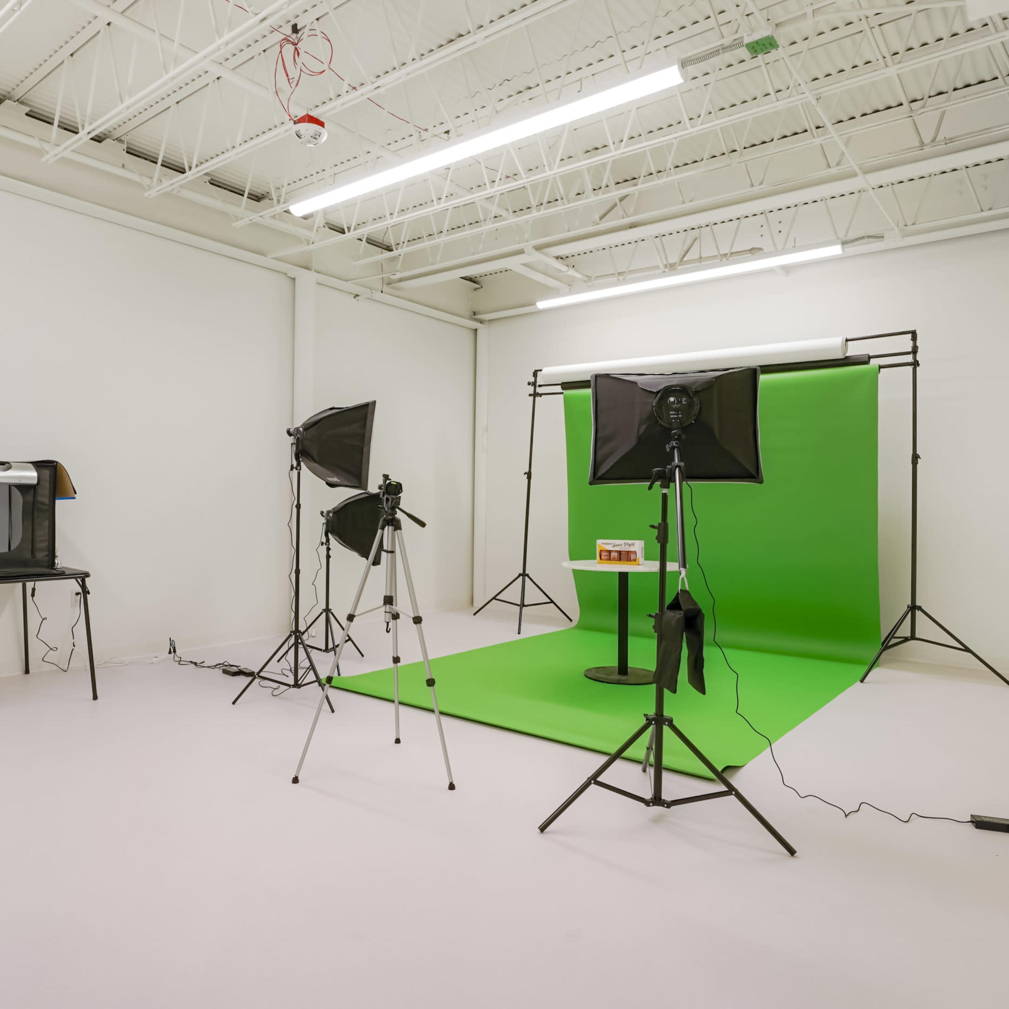 A photography studio with a green backdrop, lighting equipment, and a small table positioned in front of it.