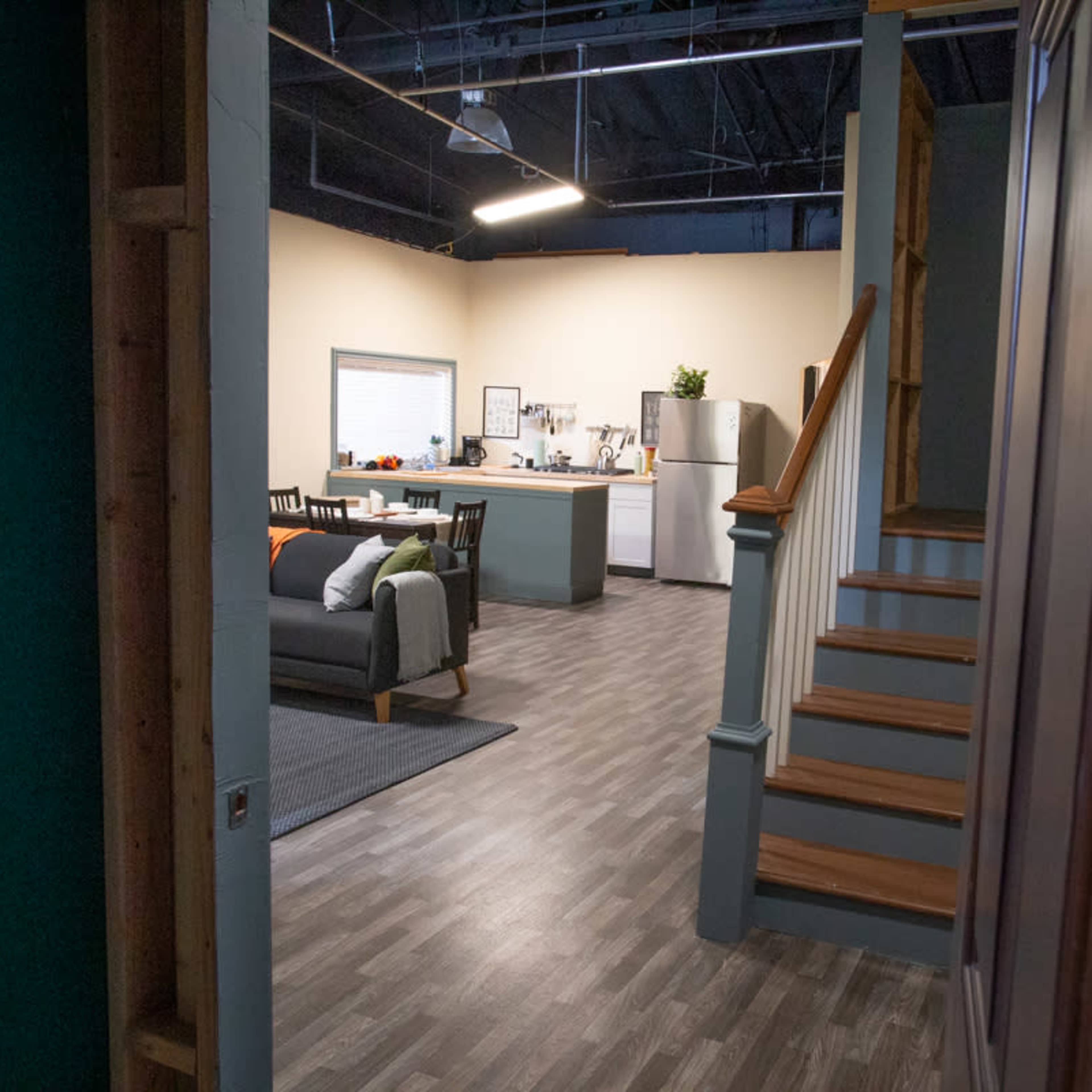 A partially constructed interior with a view into a kitchen and living area, featuring a staircase on the right.