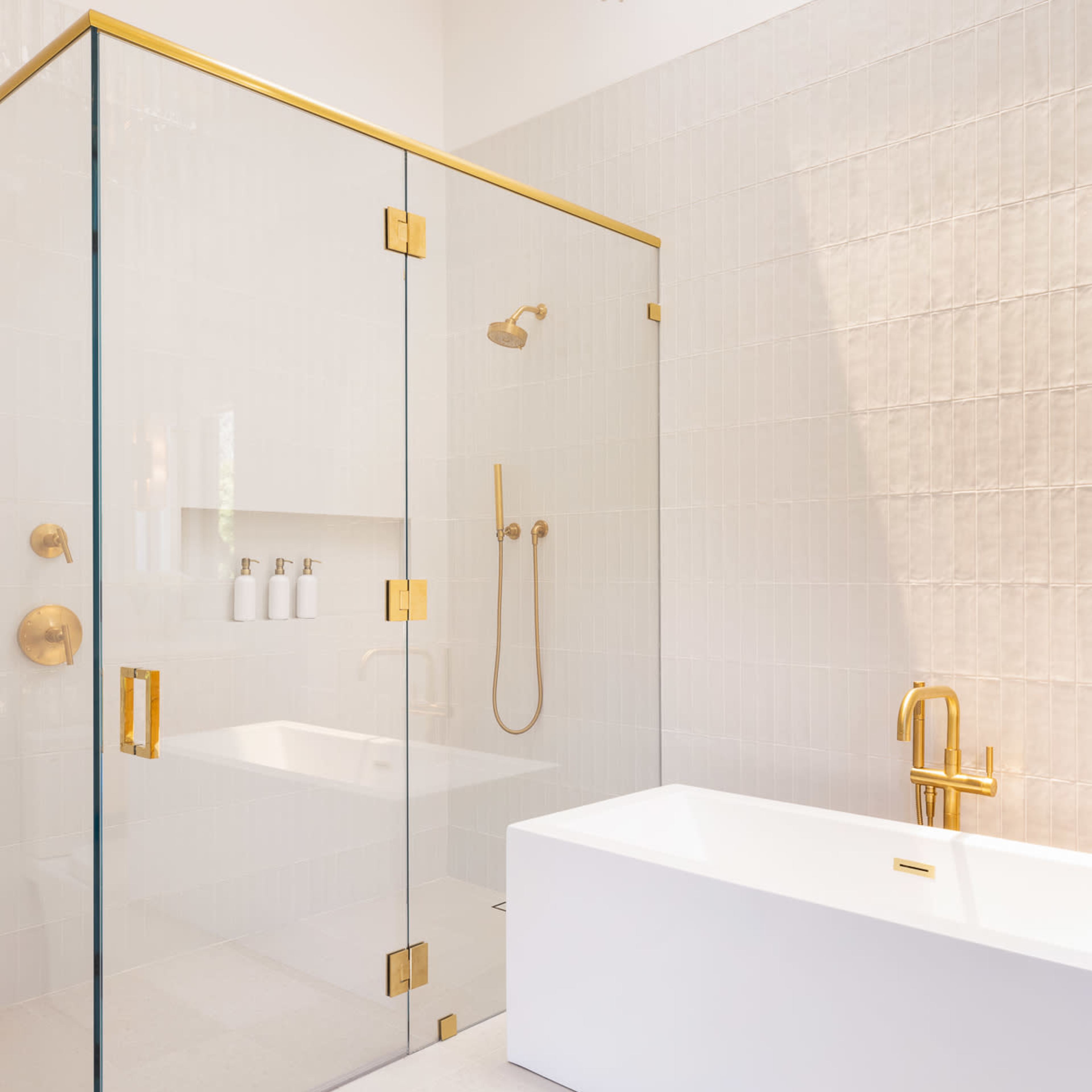 A modern bathroom features a glass shower enclosure with gold fixtures and a freestanding white bathtub.