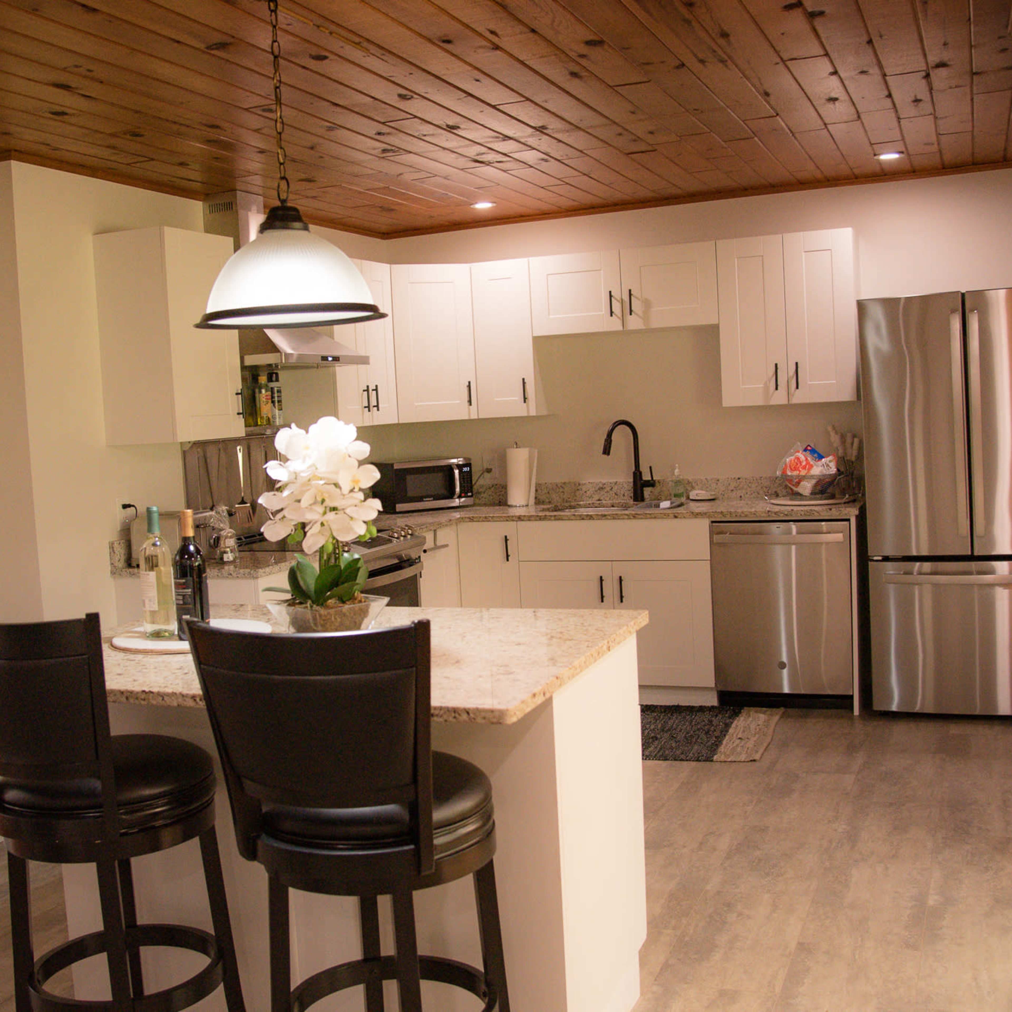 A modern kitchen features white cabinets, stainless steel appliances, and a small dining area with two black bar stools.