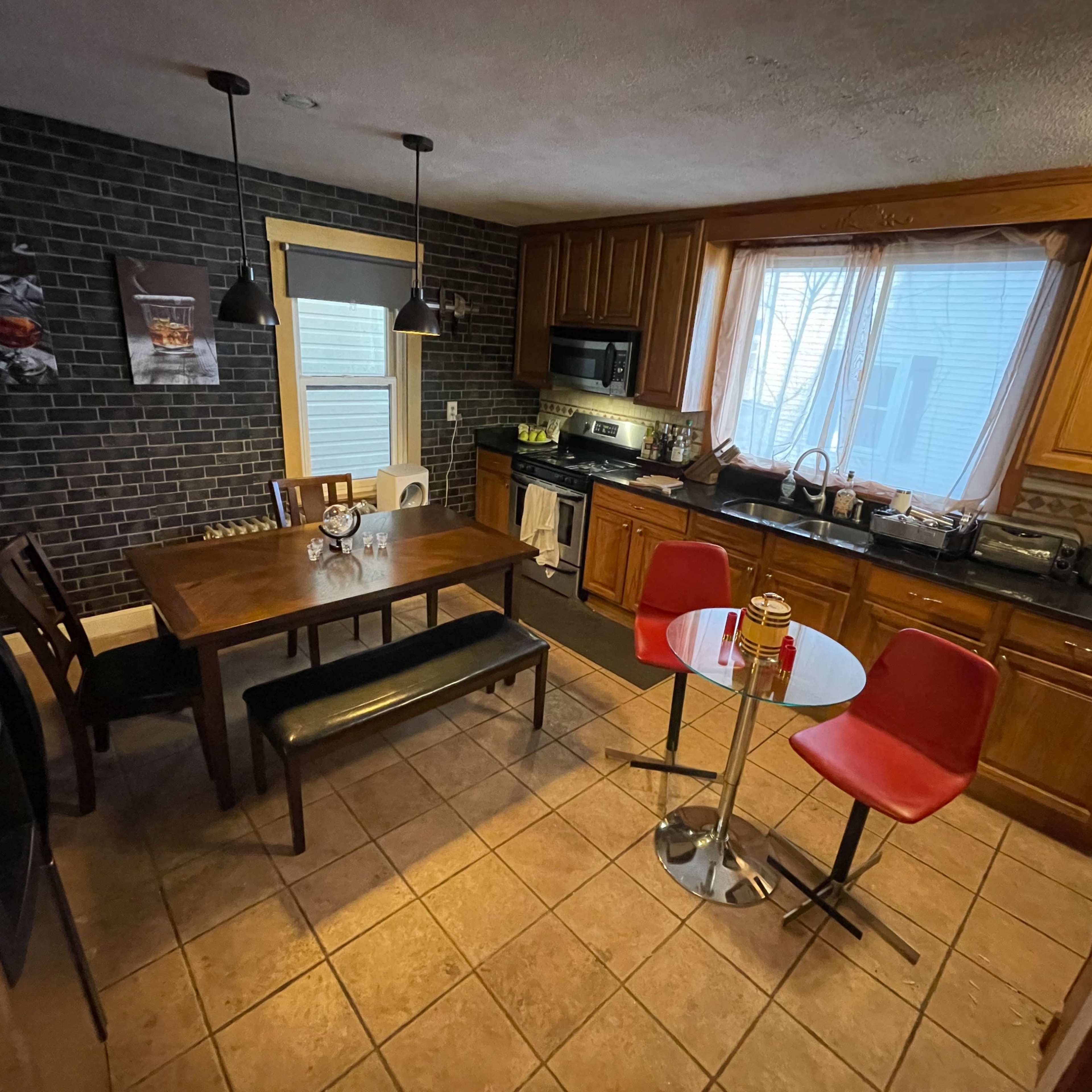 A kitchen with wooden cabinets, a black countertop, a dining table with six chairs, and a small round table with two red chairs.