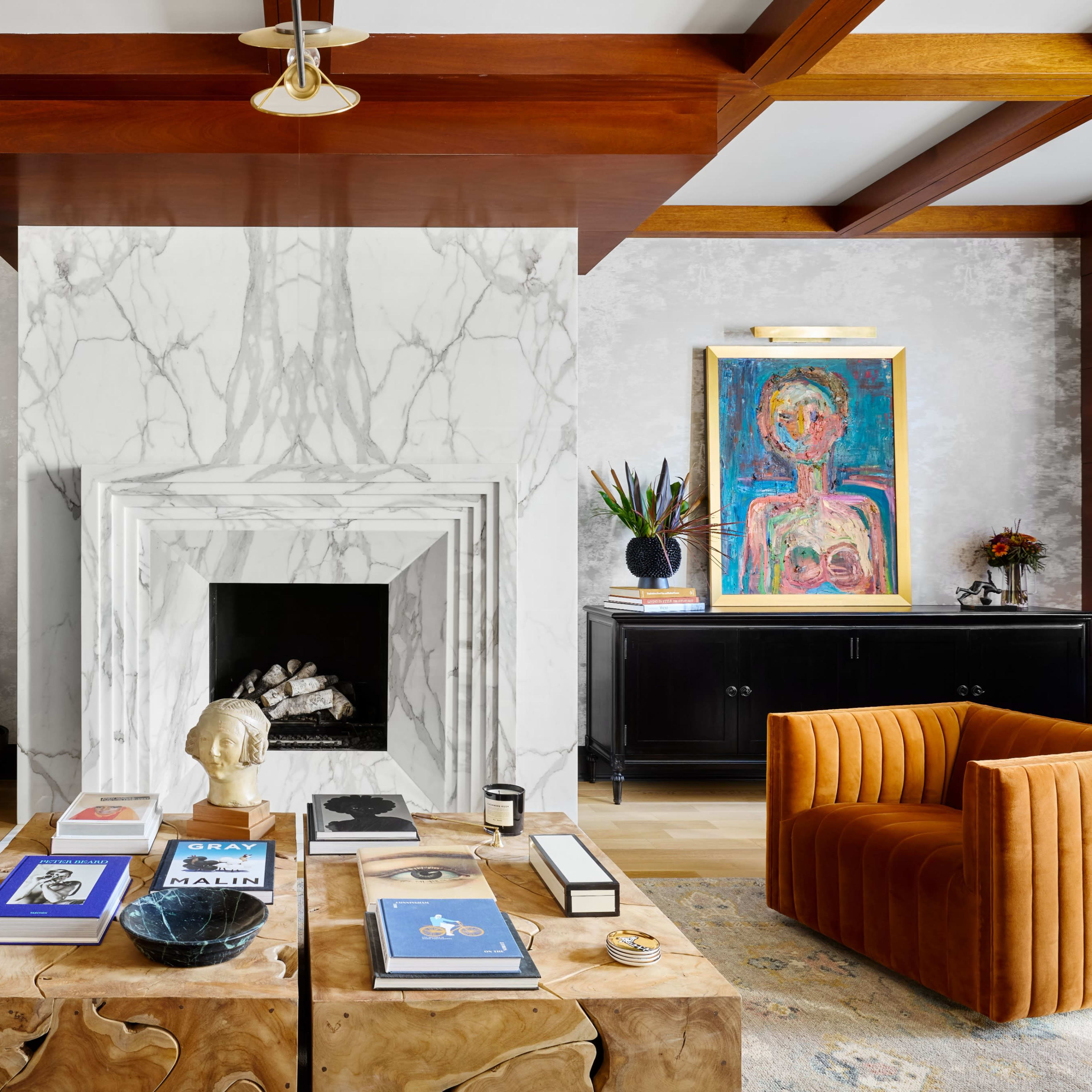A modern living room features a central fireplace with a marble surround, flanked by artwork and plants, with a coffee table adorned with books and decorative items.