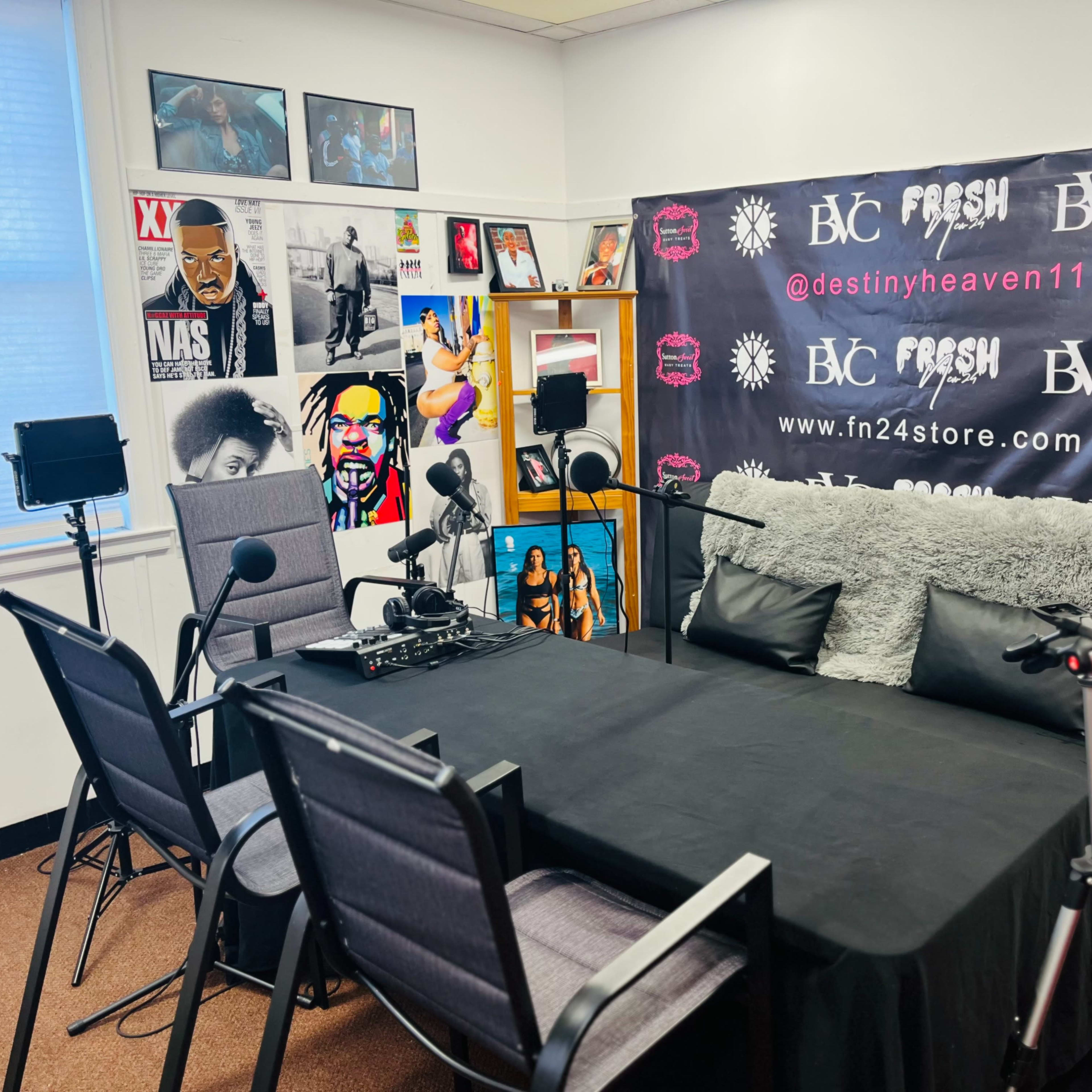 A recording studio setup with a table, microphones, and chairs, surrounded by framed posters on the walls.
