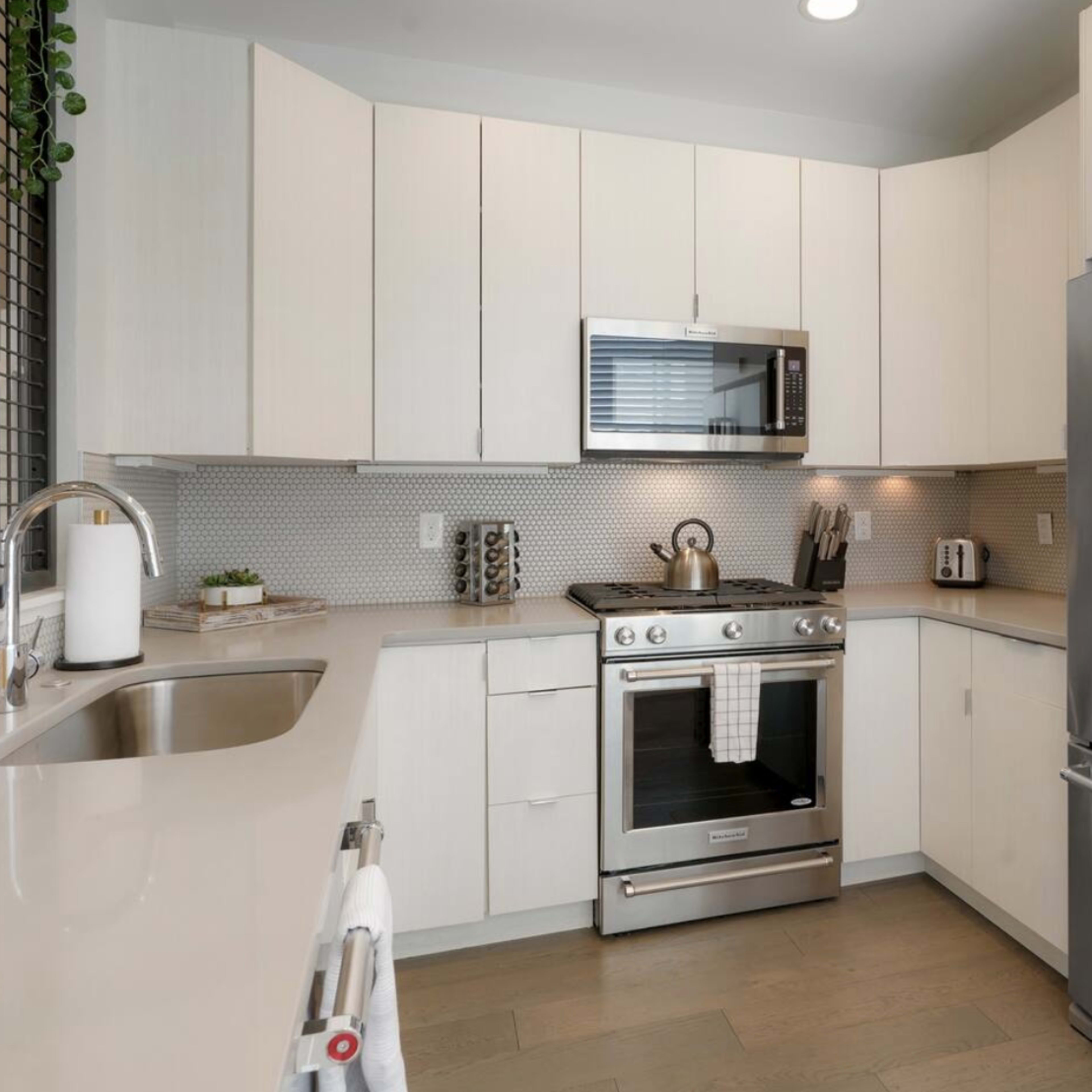 A modern kitchen with stainless steel appliances, white cabinetry, and a tiled backsplash.