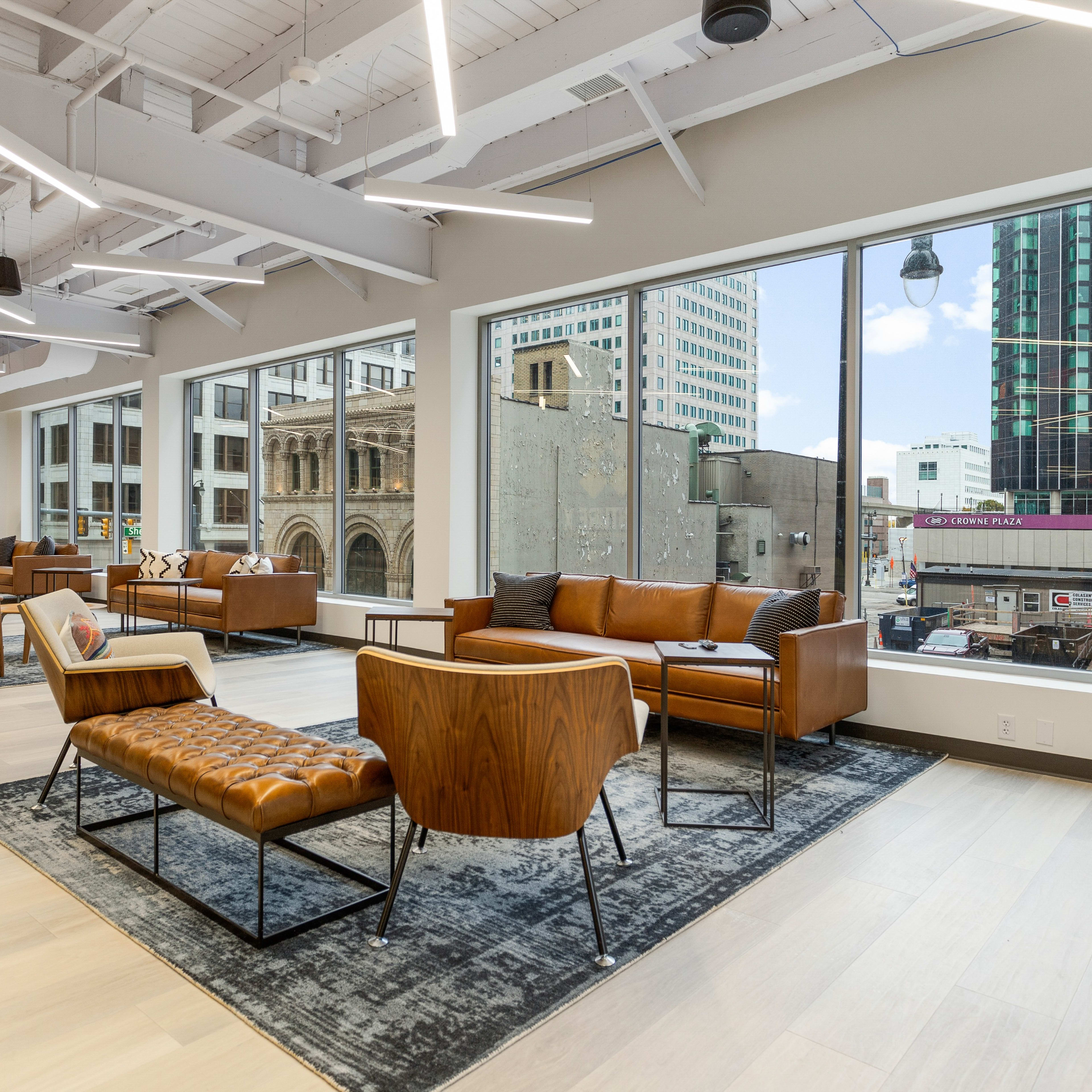 A modern lounge area with leather furniture and large windows overlooking a city street.