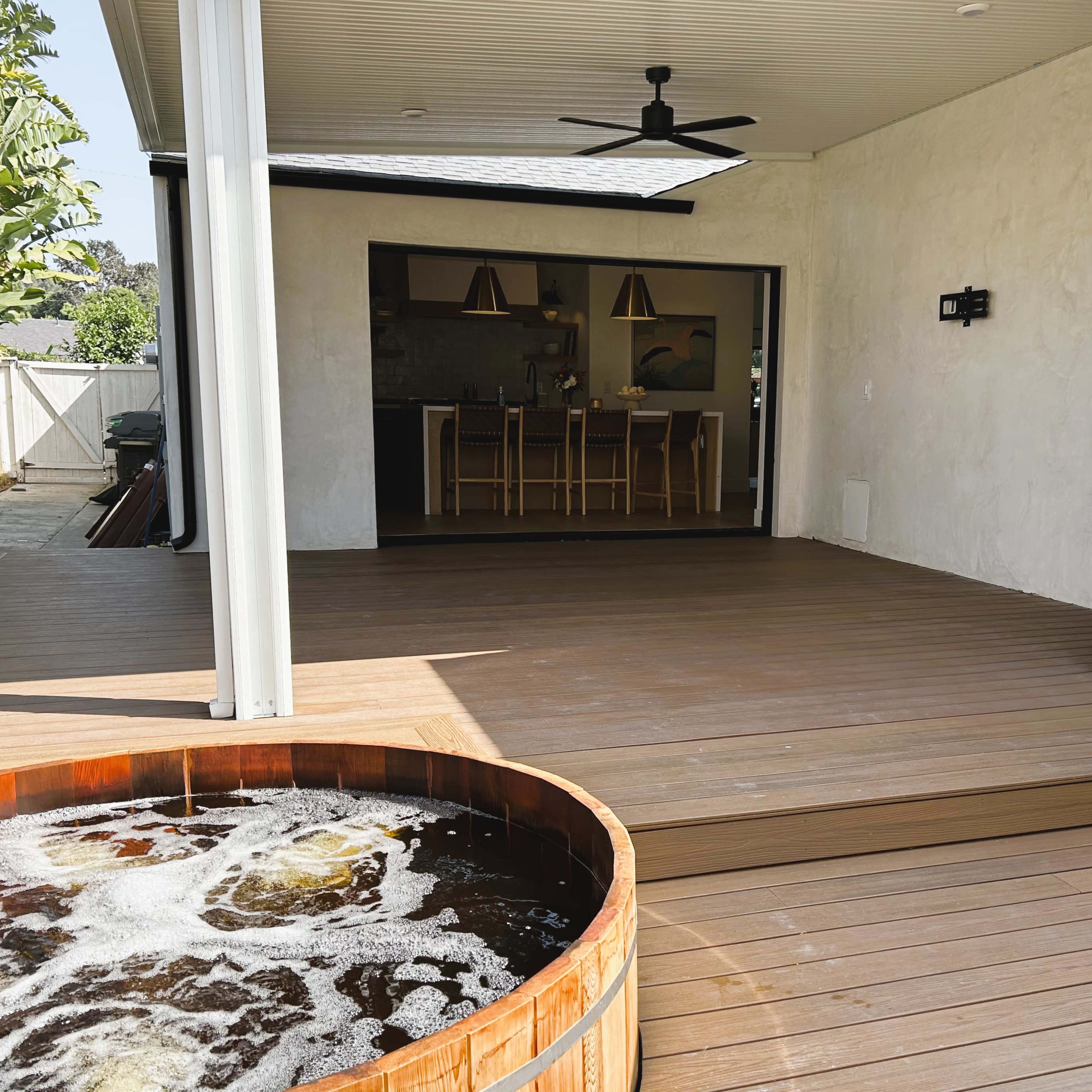 A wooden deck with a hot tub in the foreground and an outdoor kitchen area visible in the background.