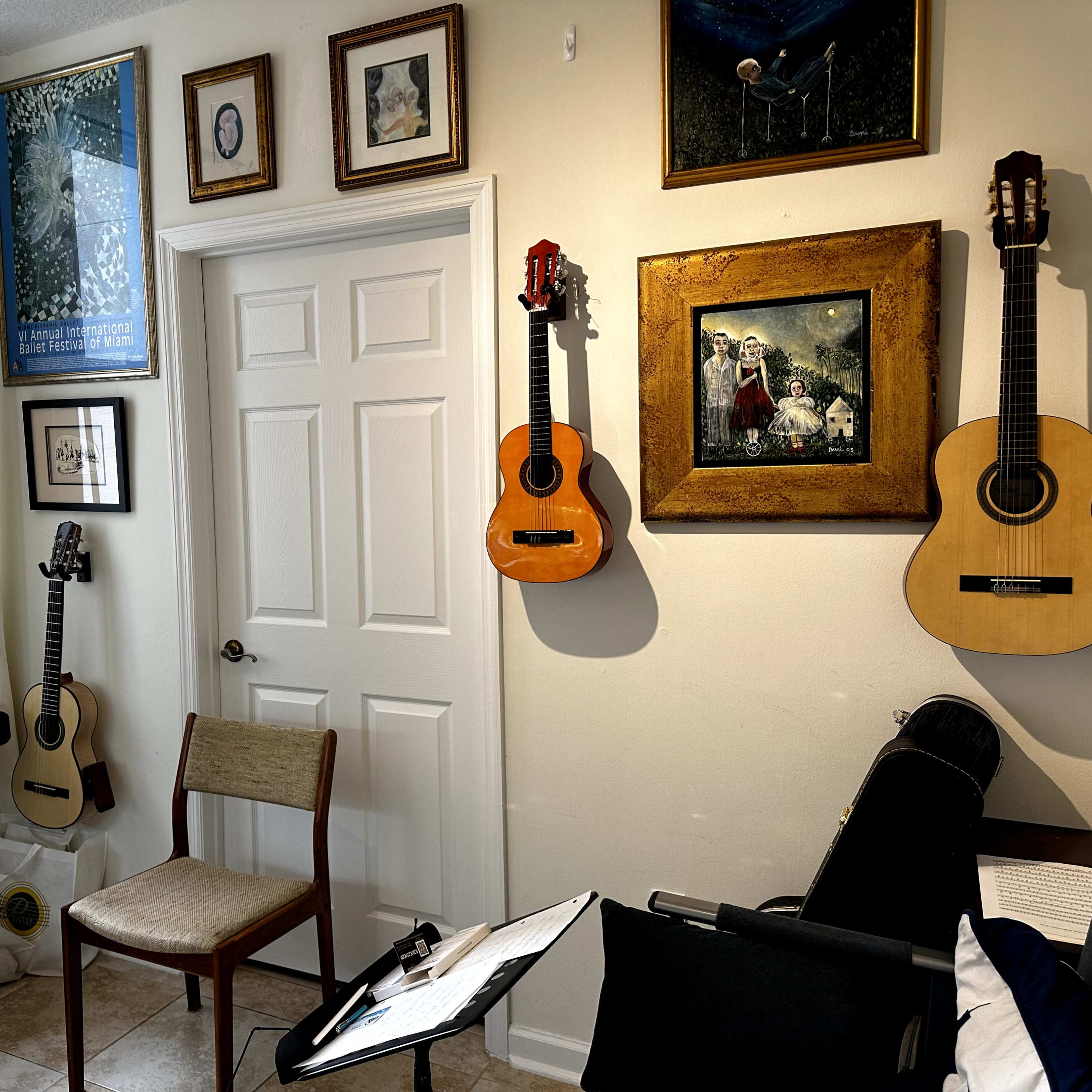 A small music room features a keyboard, two guitars hanging on the wall, a chair, and several framed pictures.