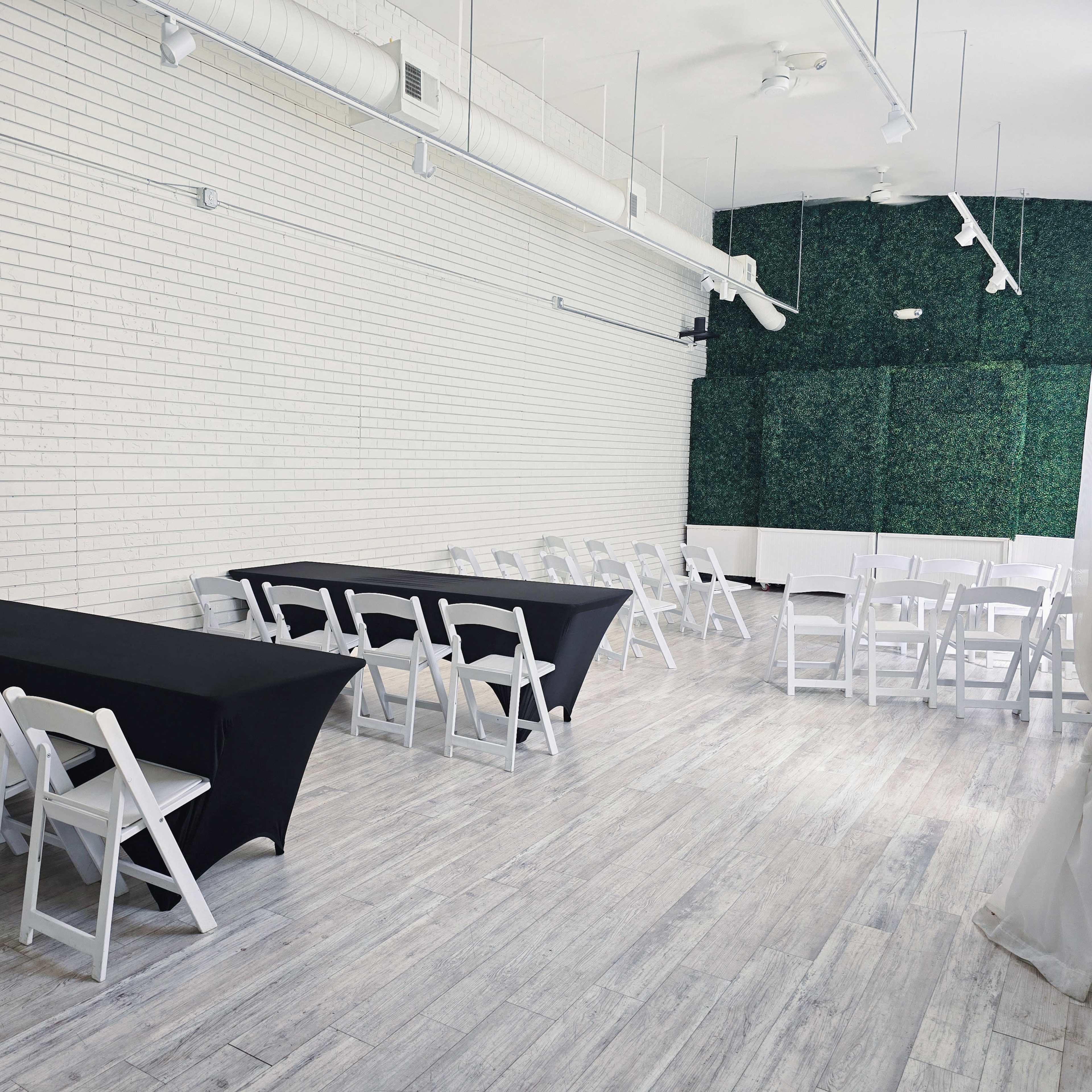 A spacious room with white walls, featuring two black tablecloth-covered tables and several white folding chairs arranged neatly.