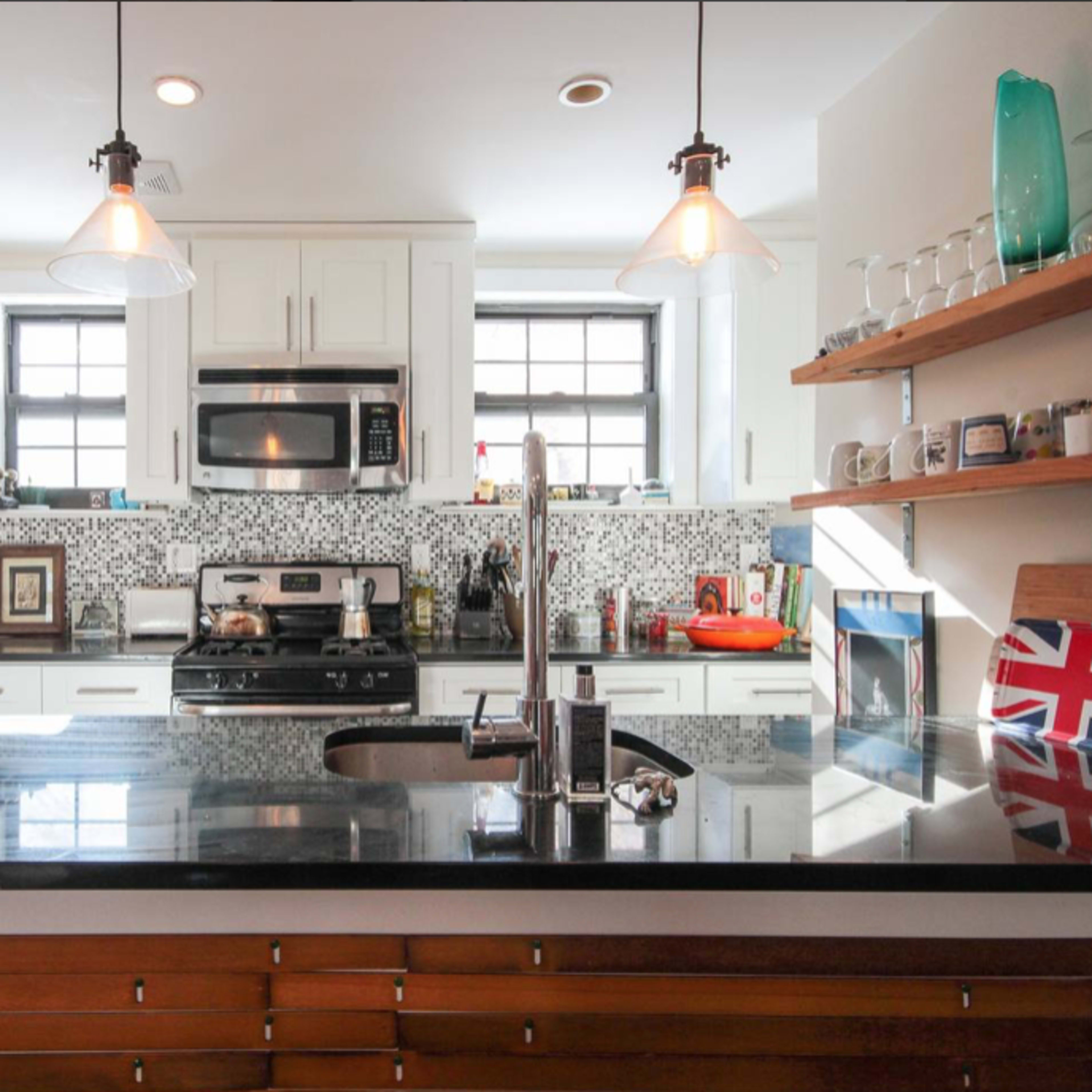 The kitchen features white cabinetry, a dark countertop, and modern appliances, with a striking patterned backsplash and wooden shelves displaying various items.