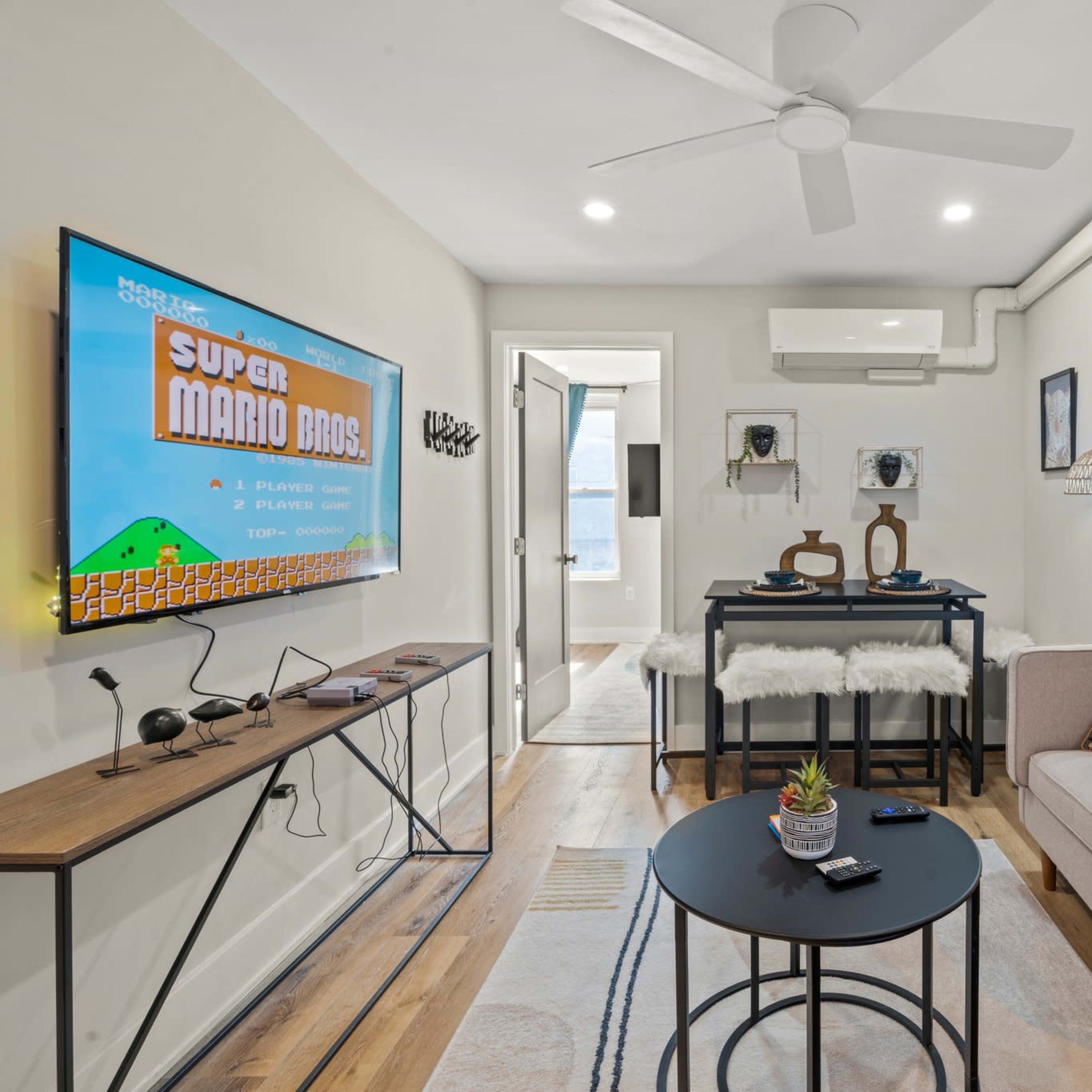 A modern living room featuring a wall-mounted TV displaying a classic video game, a coffee table, and a sofa adorned with decorative pillows.