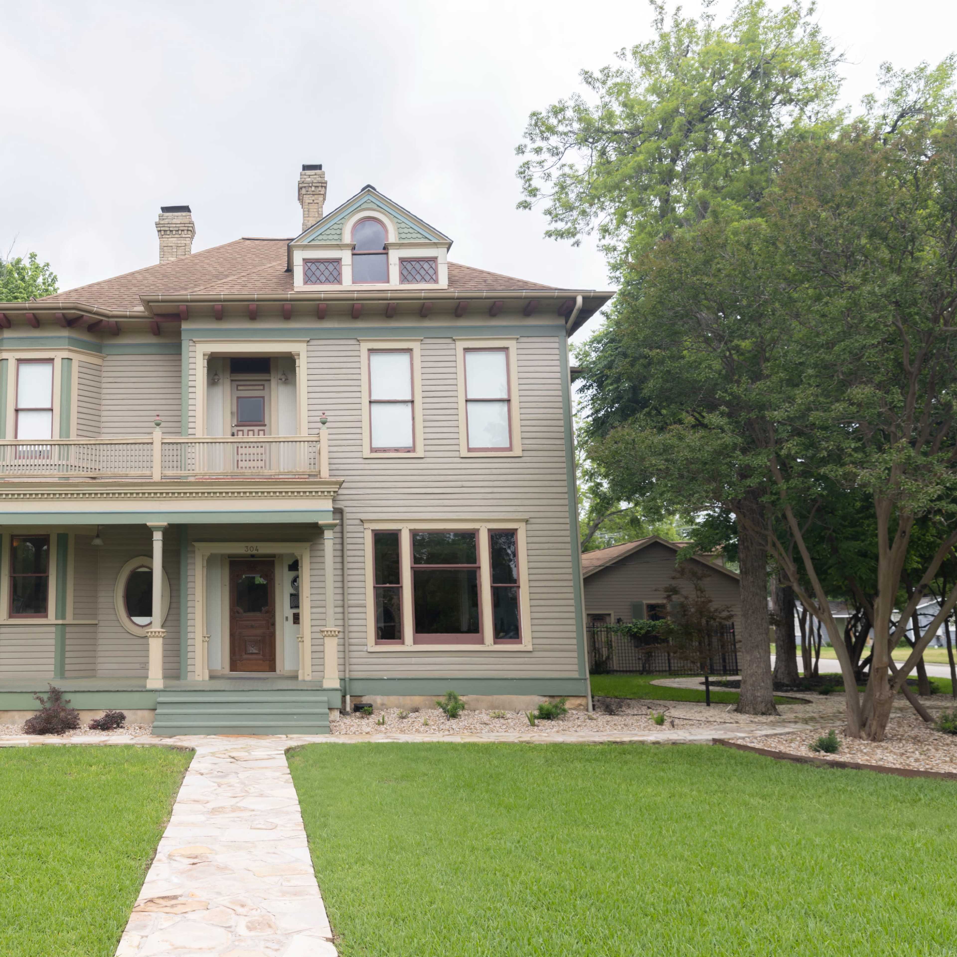 A large, two-story Victorian-style house with a wraparound porch and a neatly landscaped front yard.