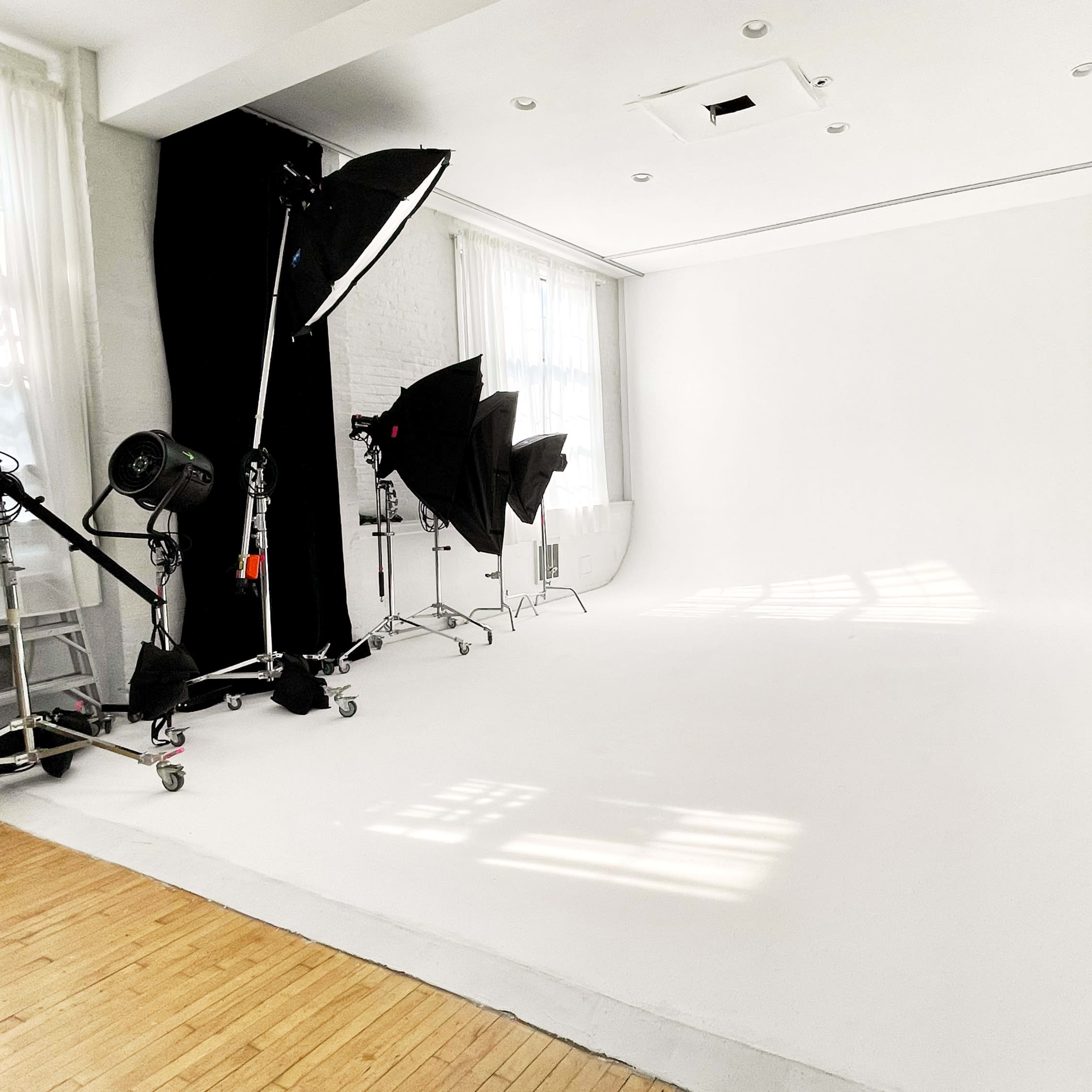 A photography studio with a large white backdrop, various lighting equipment, and dark curtains.