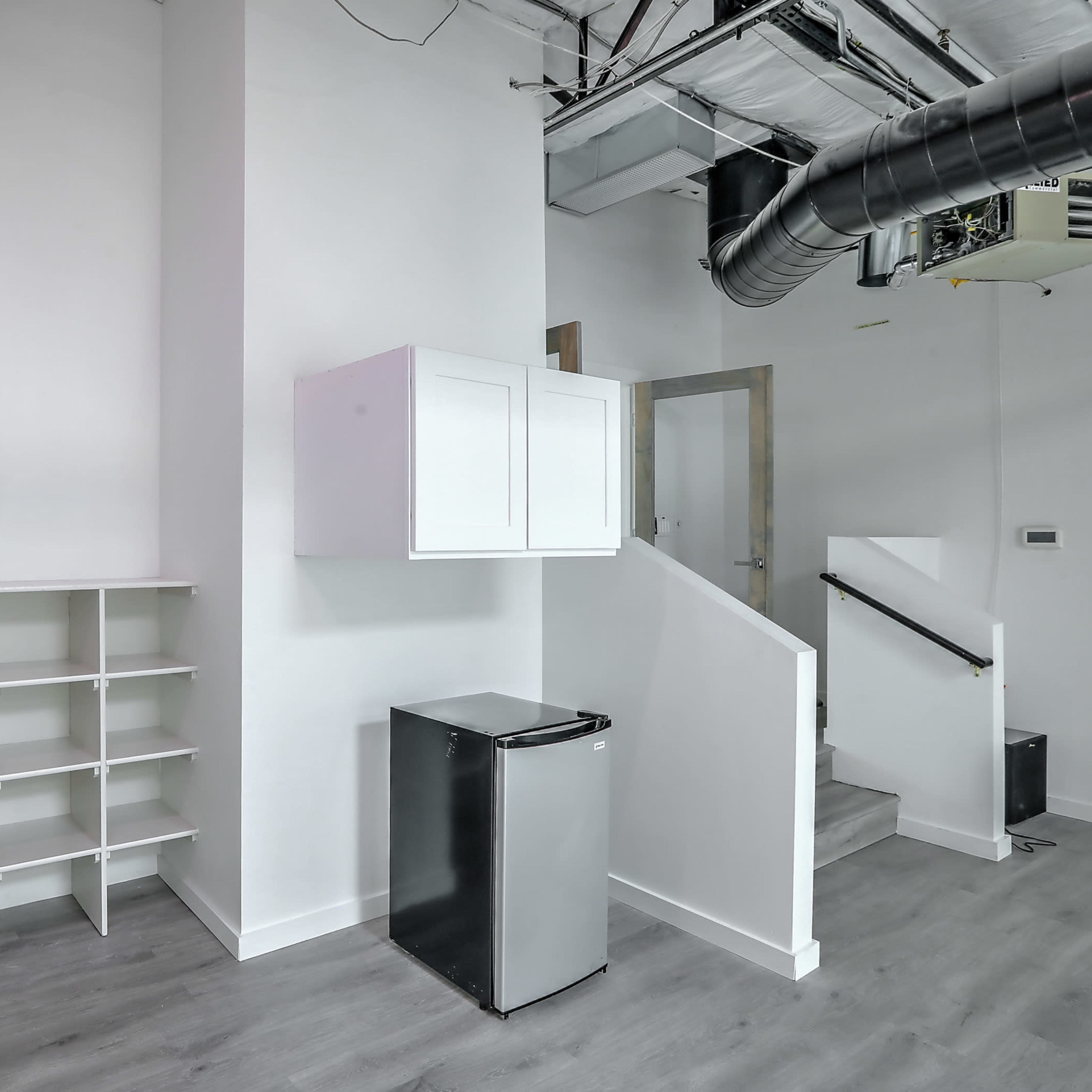 A small, modern room featuring a white shelving unit, a refrigerator, and a staircase.