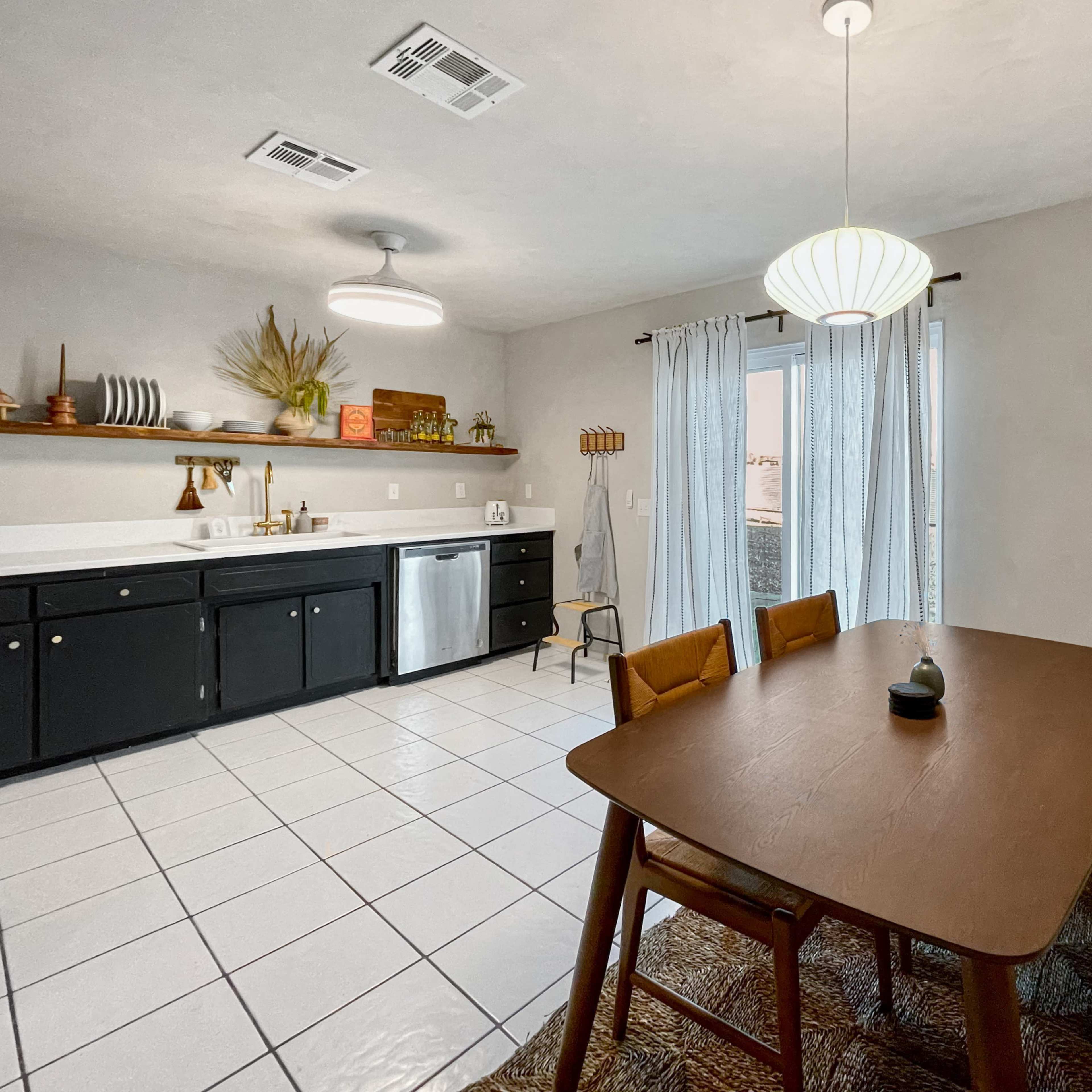 A modern kitchen with a dining area featuring a wooden table, bench seating, and white tile flooring.