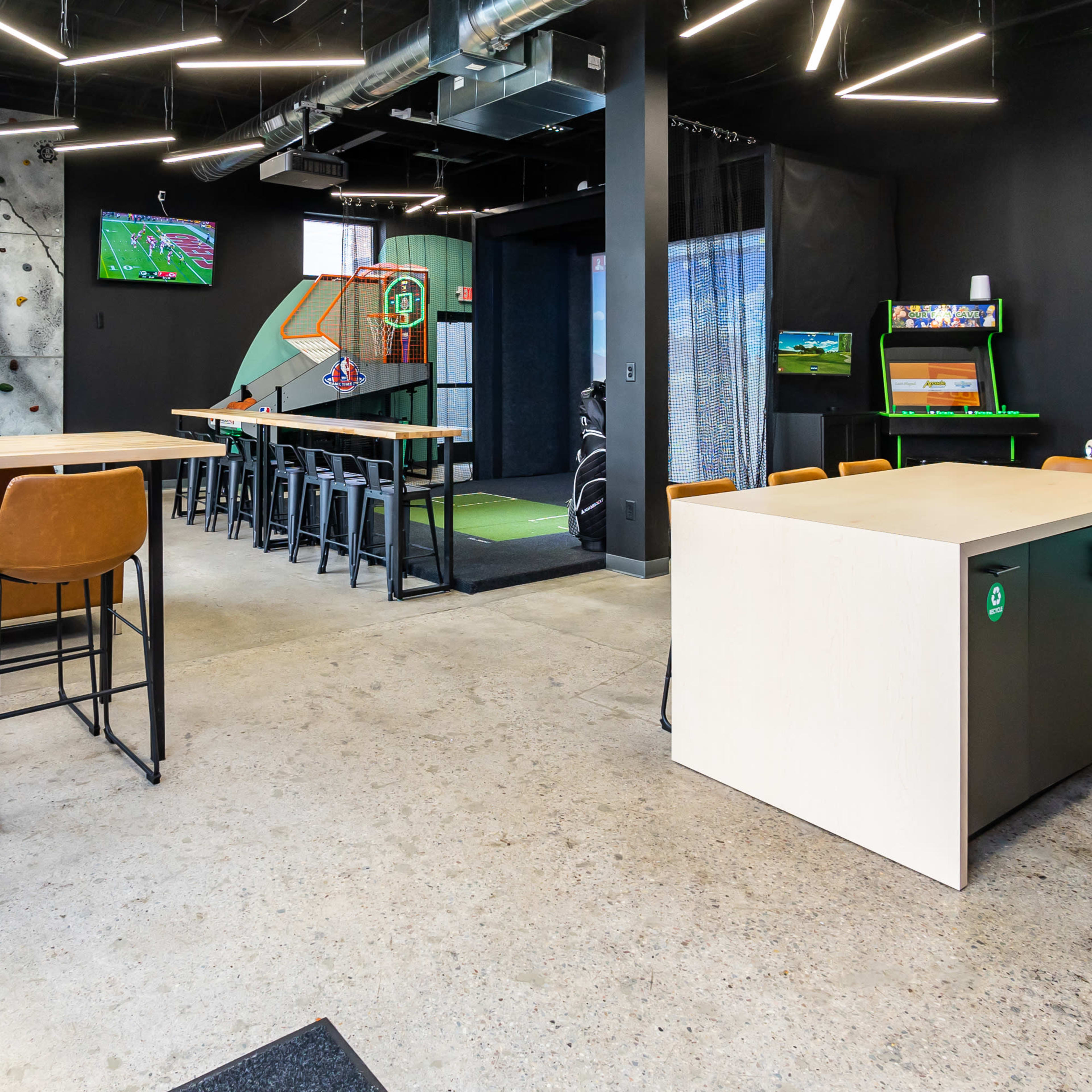 A modern recreational space featuring a climbing wall, sports screens, and various seating arrangements.