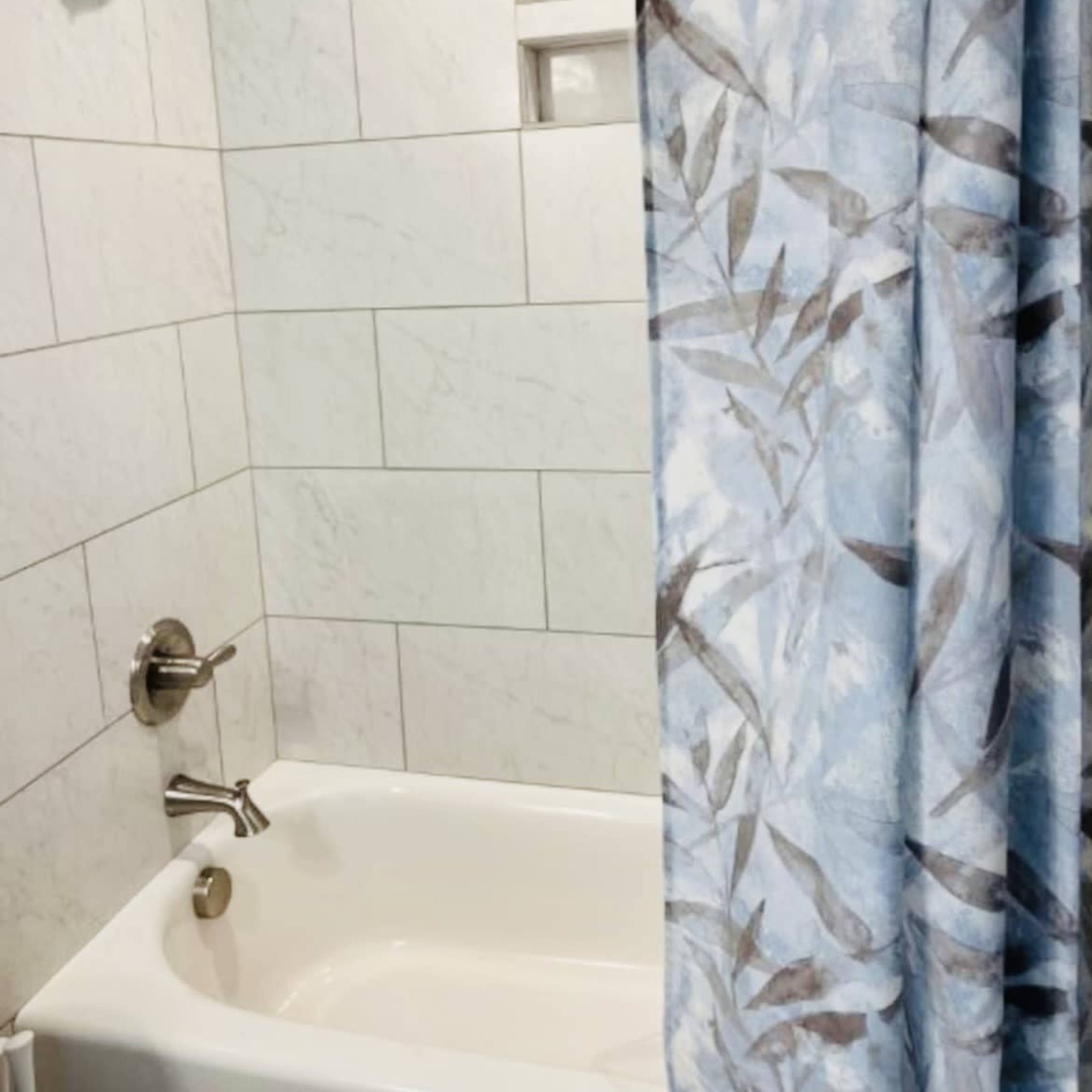 A bathroom features a bathtub with a showerhead and a patterned curtain partially drawn to the side.