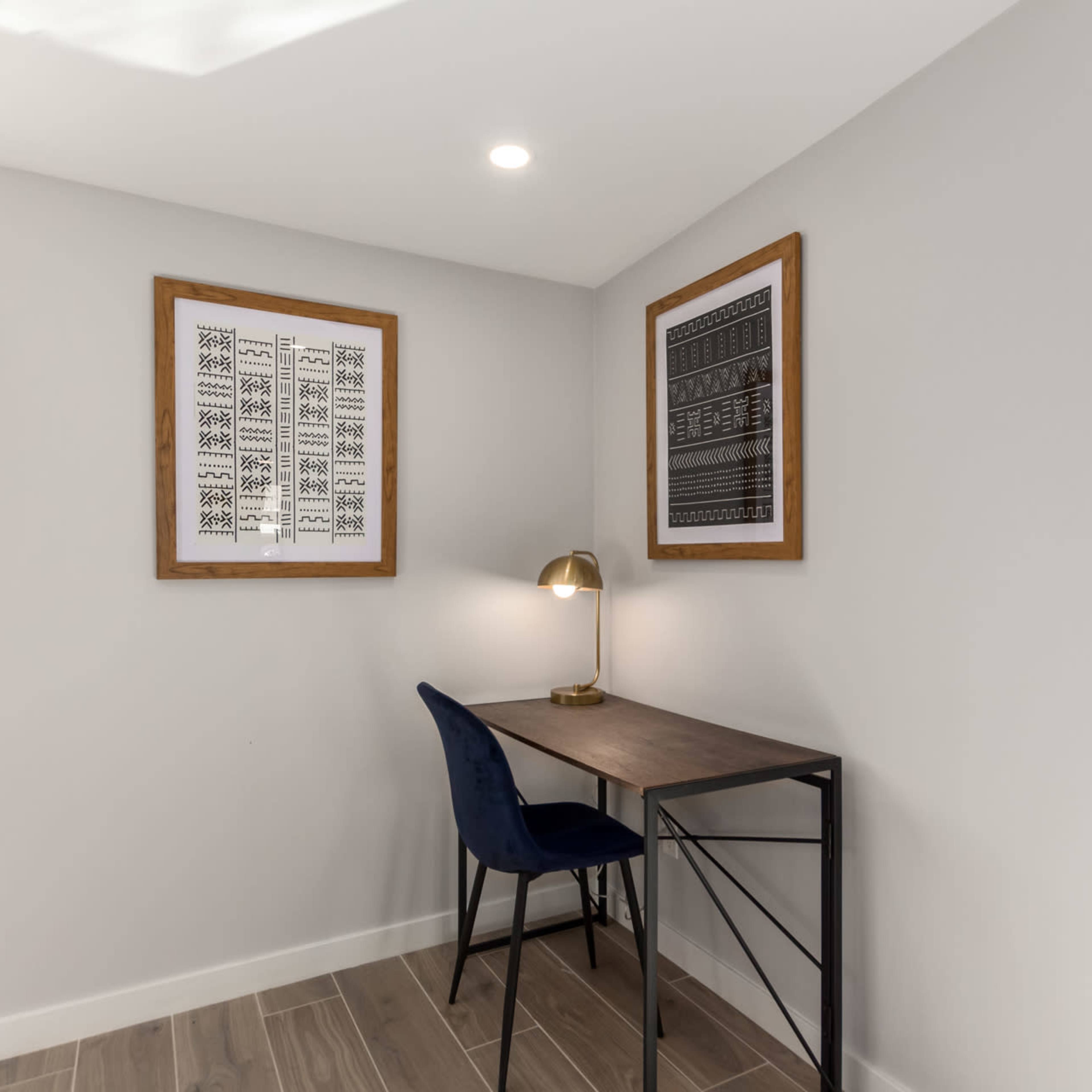 A small corner office space with a wooden desk, a blue chair, and framed artwork on the walls.