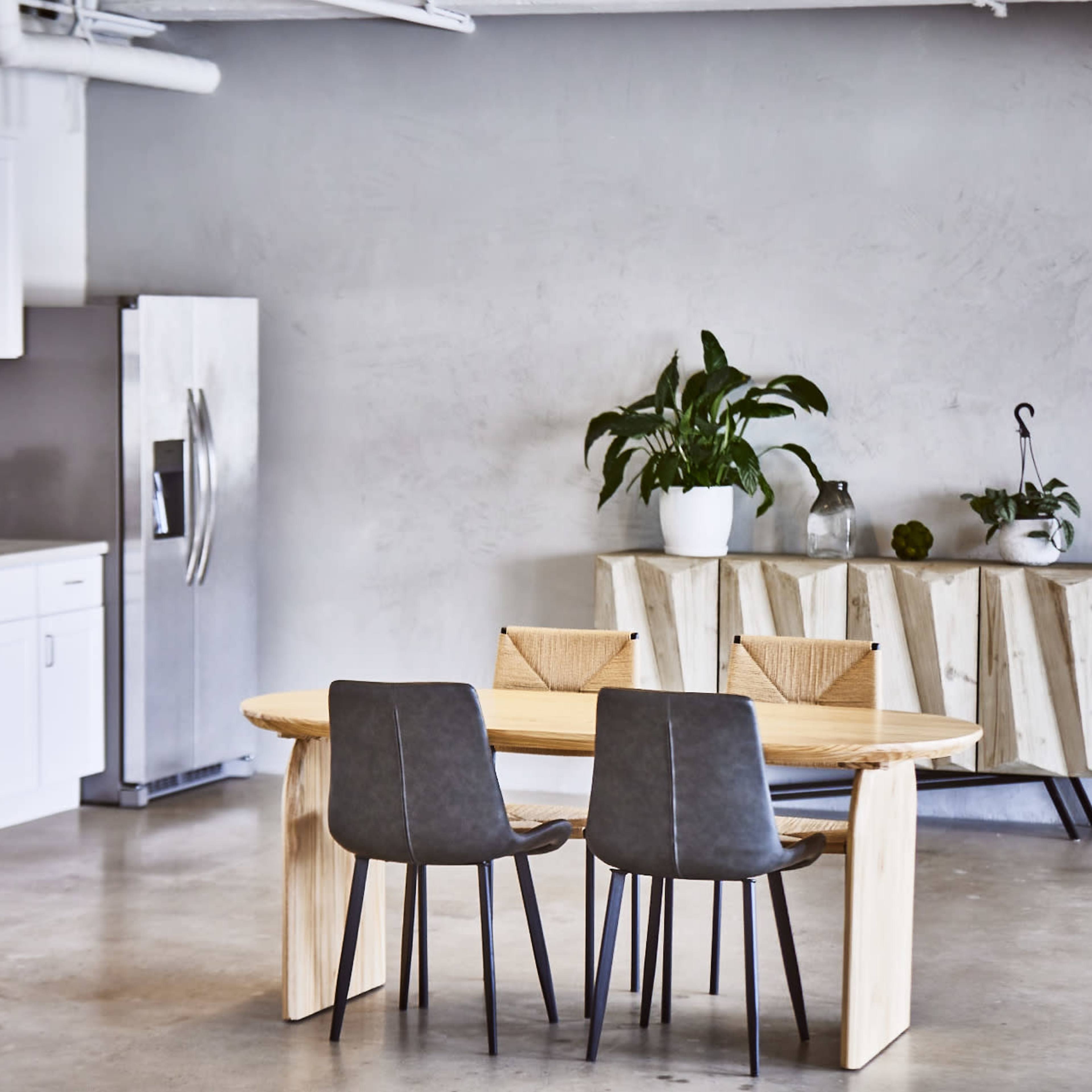 A modern kitchen and dining area features a wooden table with two chairs, stainless steel appliances, and a minimalist decor in shades of gray and white.