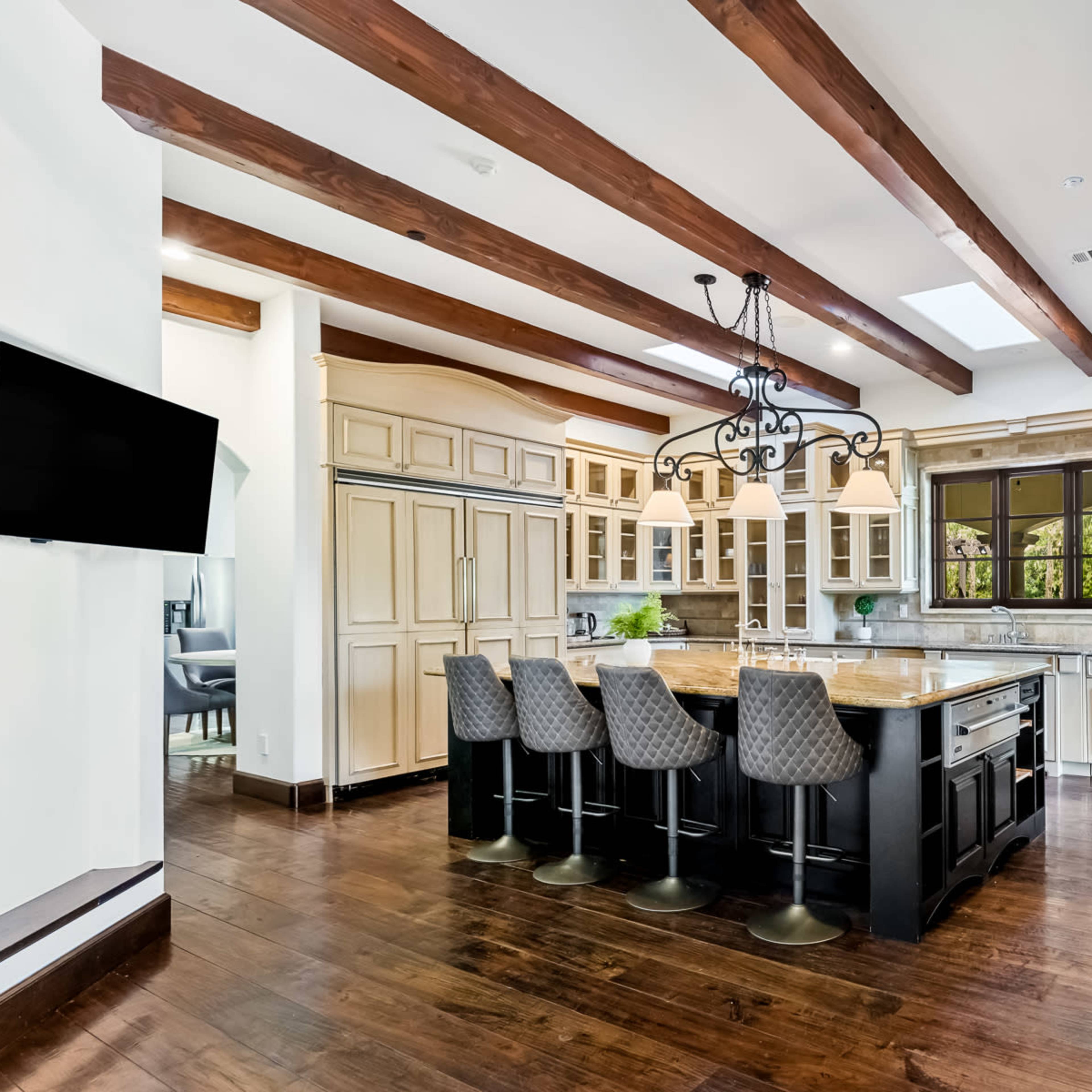 A spacious kitchen features an island with seating, sleek cabinetry, and wooden beams on the ceiling.
