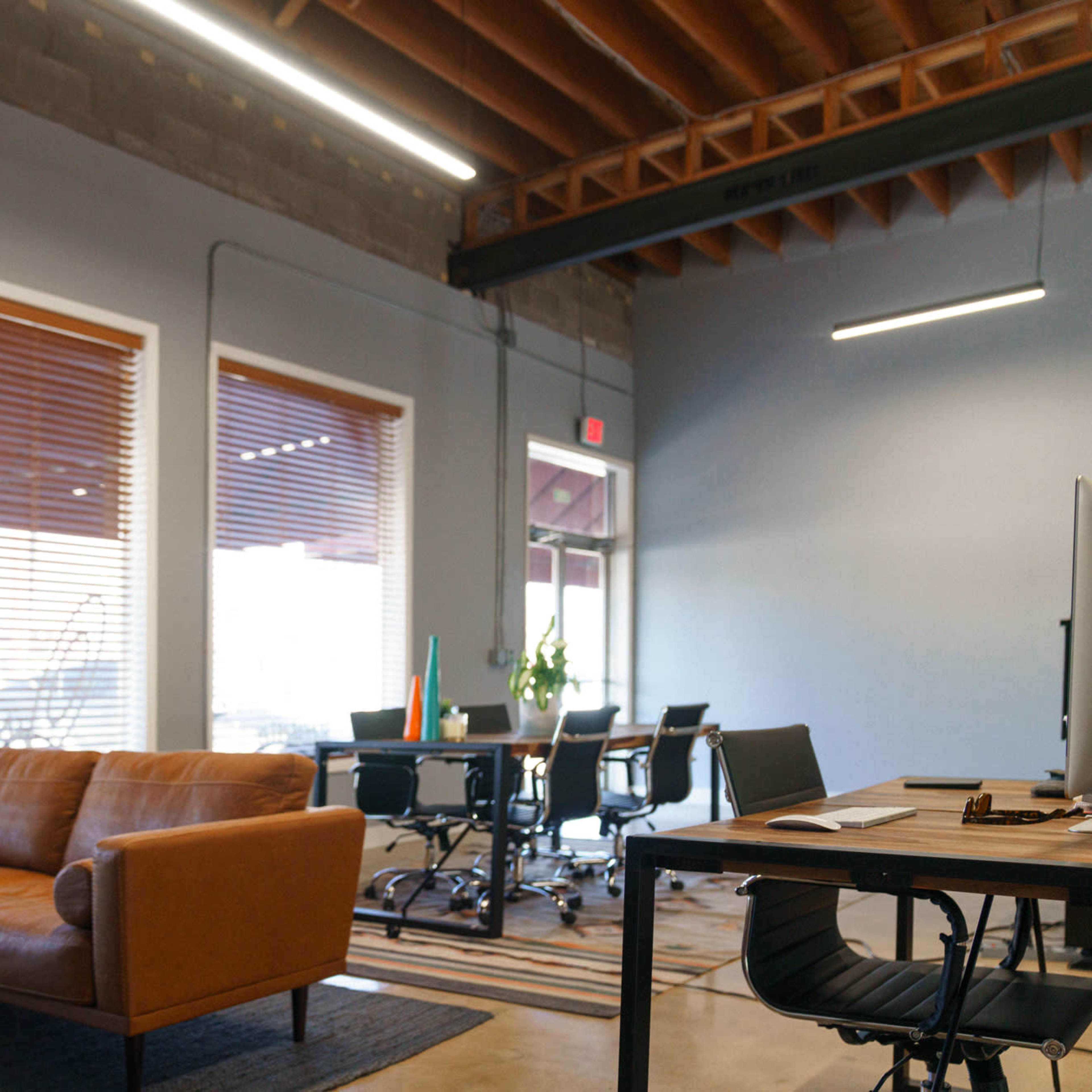 A modern office space with a brown leather sofa, a dark rug, and a workspace equipped with a desk and chairs.