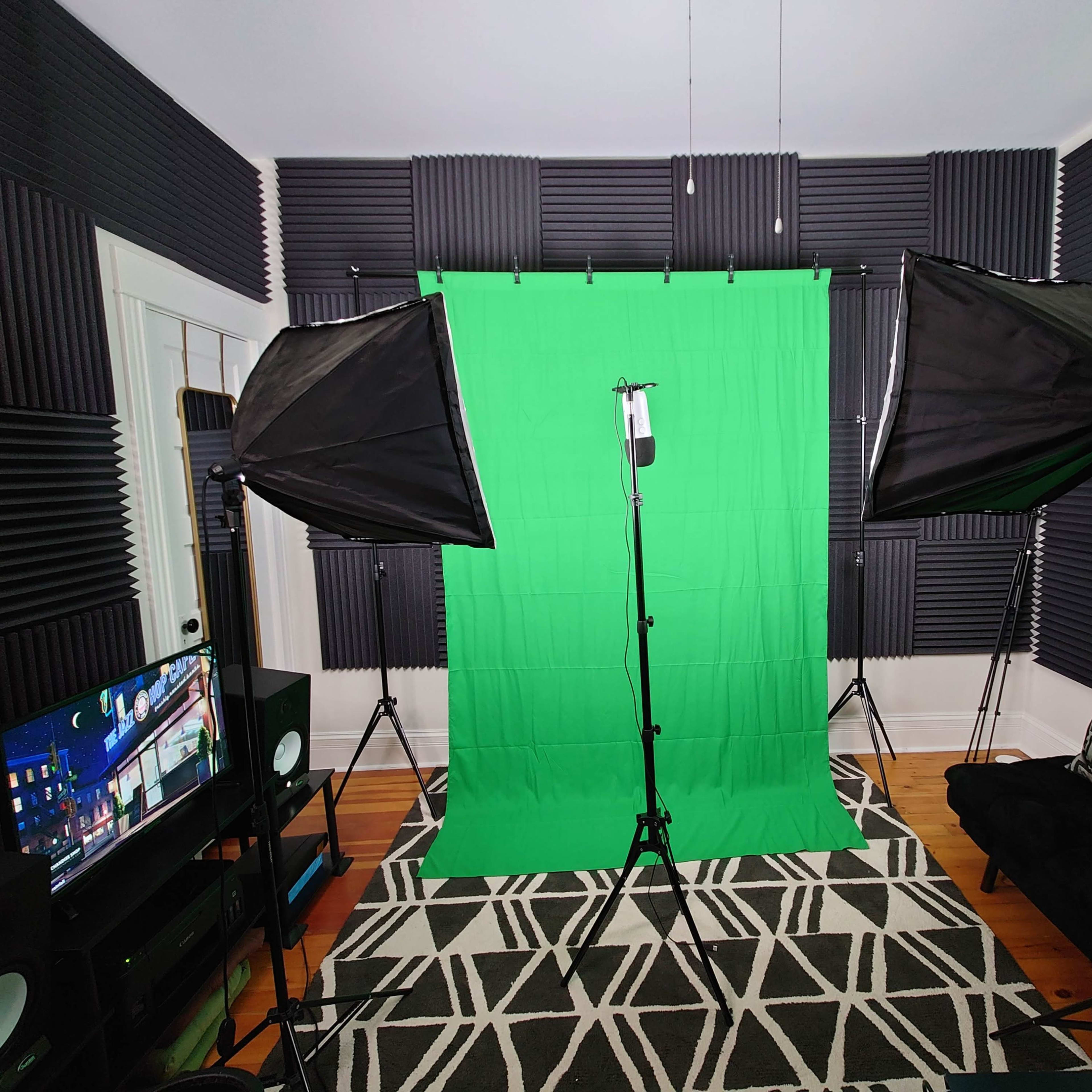 A photography studio setup features a green backdrop surrounded by softbox lights, with a television and a couch in the room.