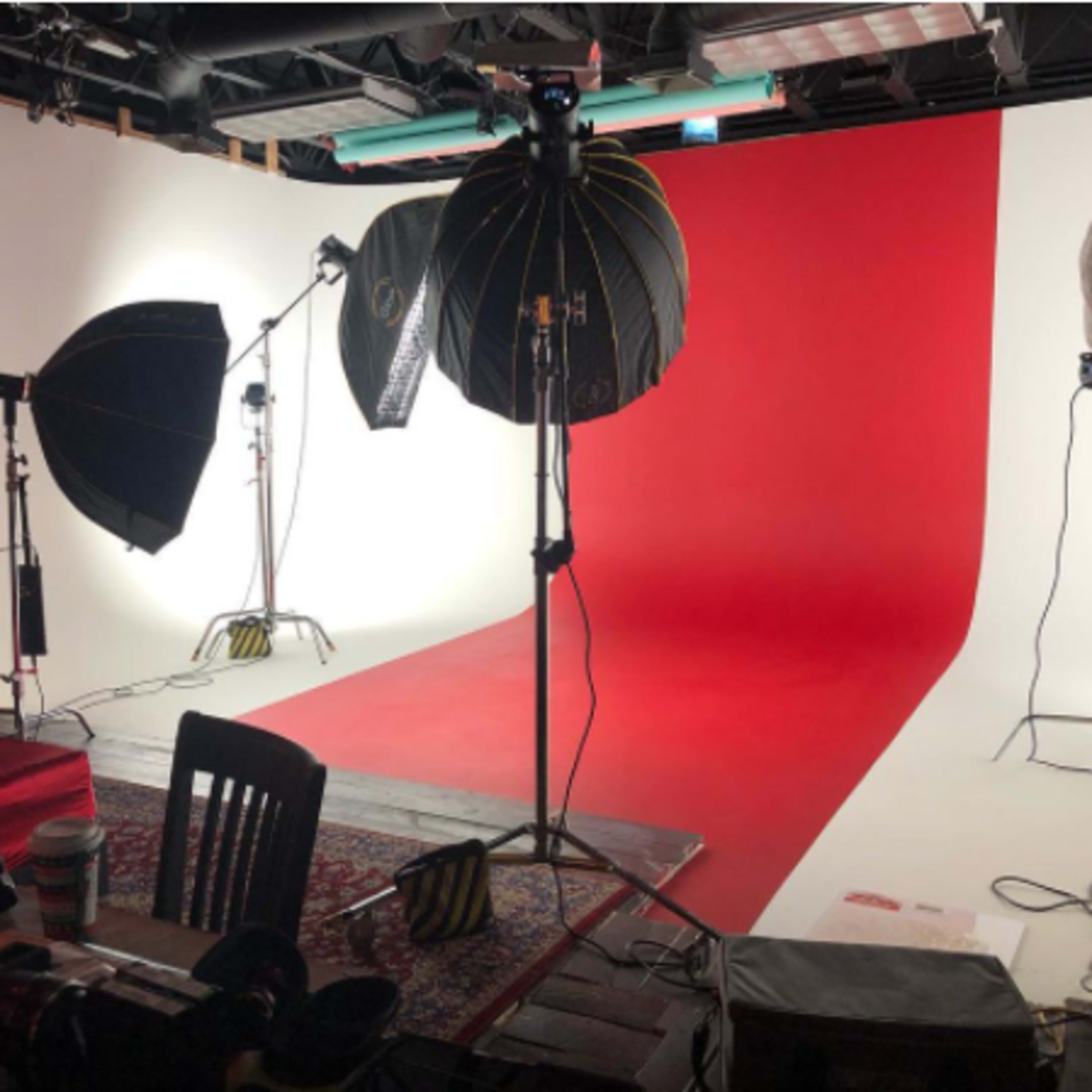 A photo studio setup with two large softbox lights positioned in front of a red and white backdrop, along with equipment on a table in the foreground.