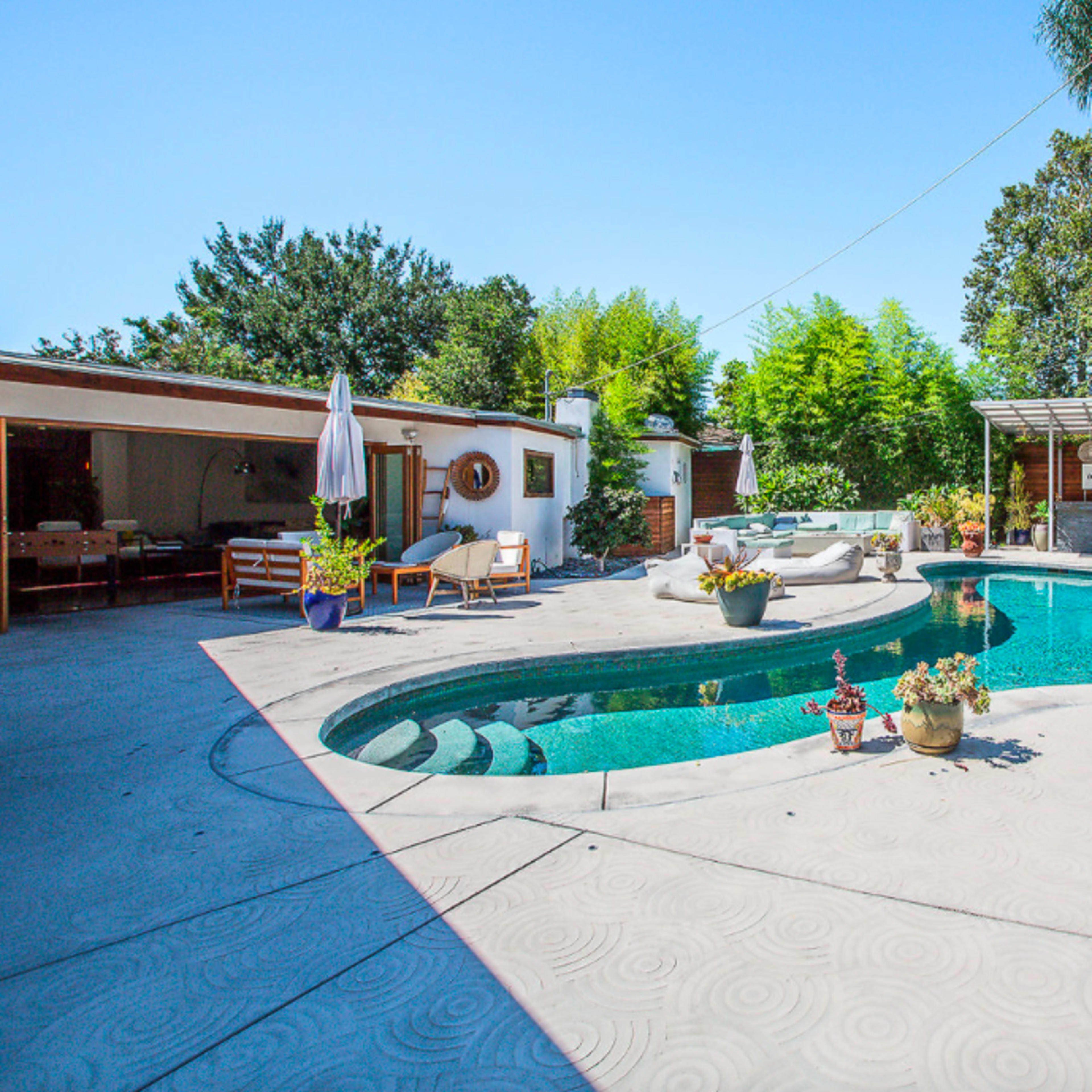 A backyard with a shaped swimming pool surrounded by landscaped greenery and outdoor seating areas.