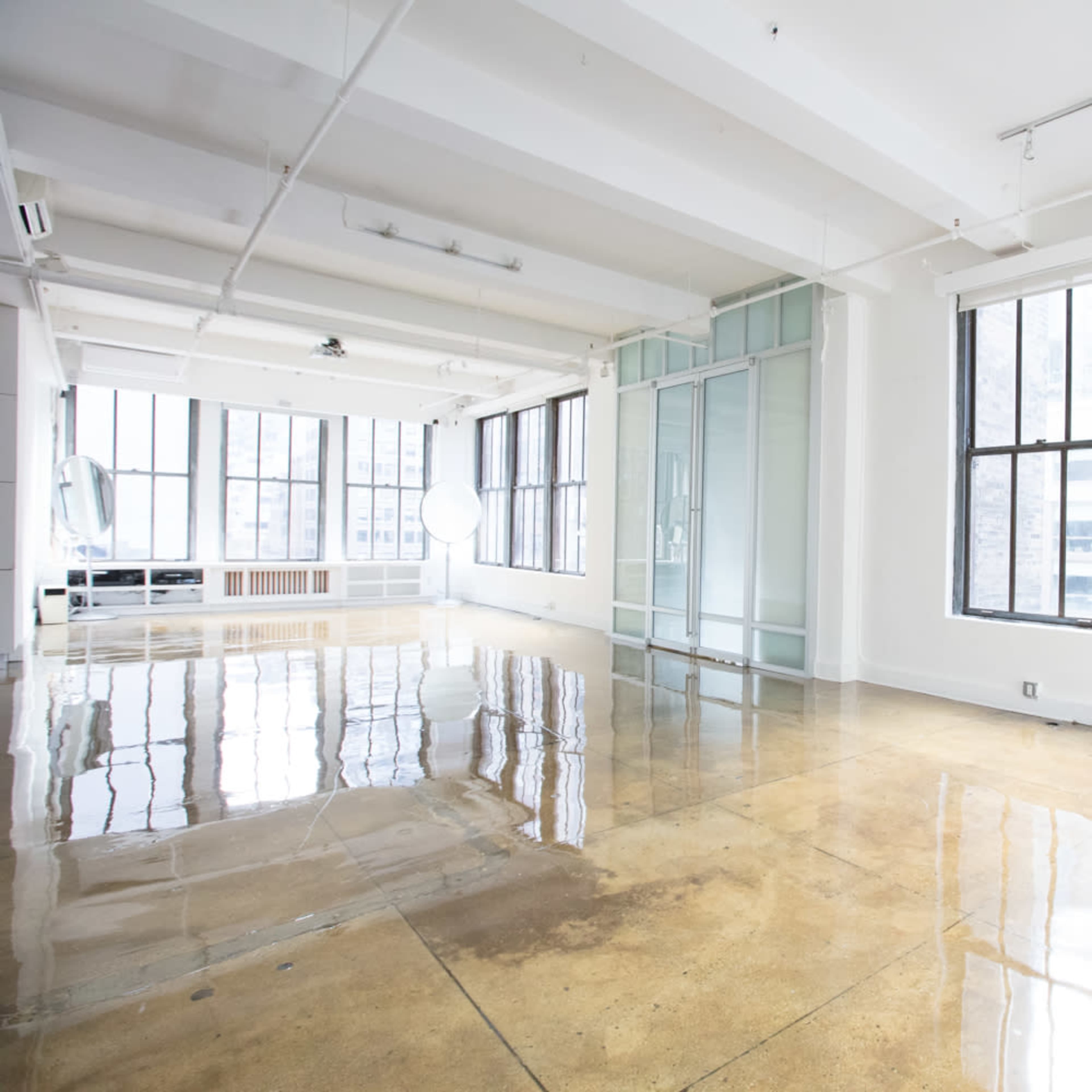 A spacious, empty room with high ceilings and reflective polished concrete floors, featuring large windows that allow natural light to fill the space.
