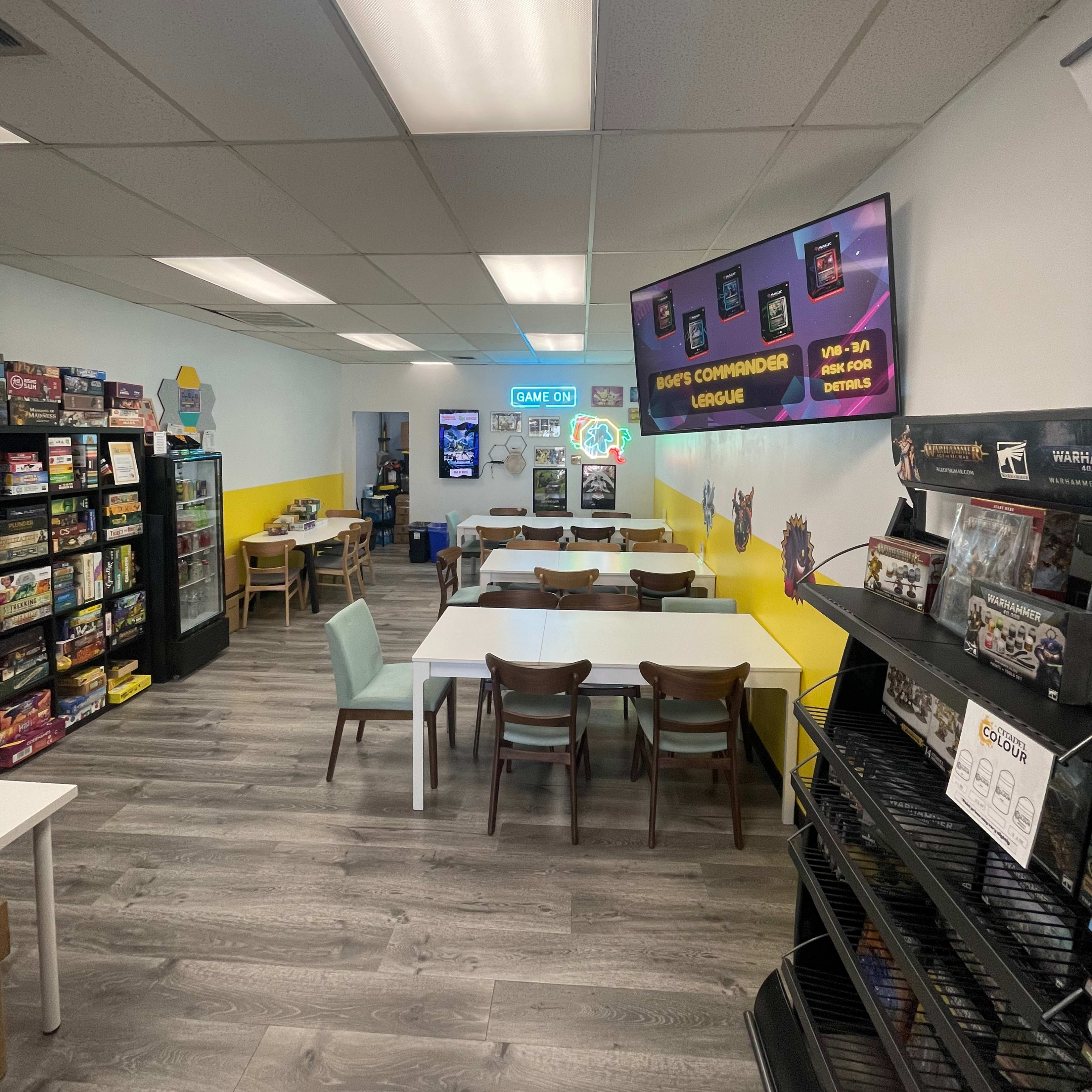 The interior of a brightly colored game store featuring tables for events, shelves of board games, and promotional displays on the walls.