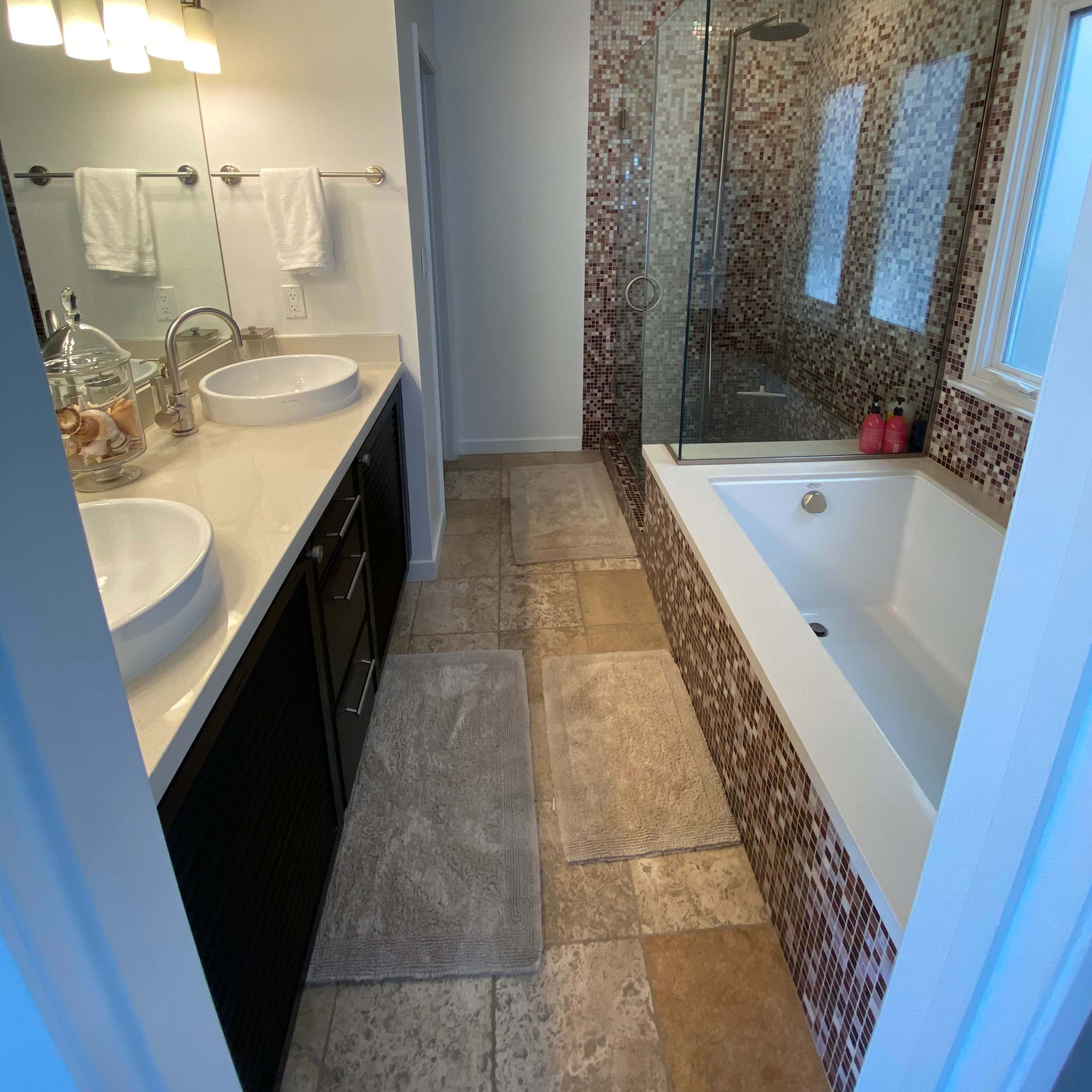 A modern bathroom featuring a double sink vanity, a glass shower enclosure, and a tub surrounded by mosaic tile accents.