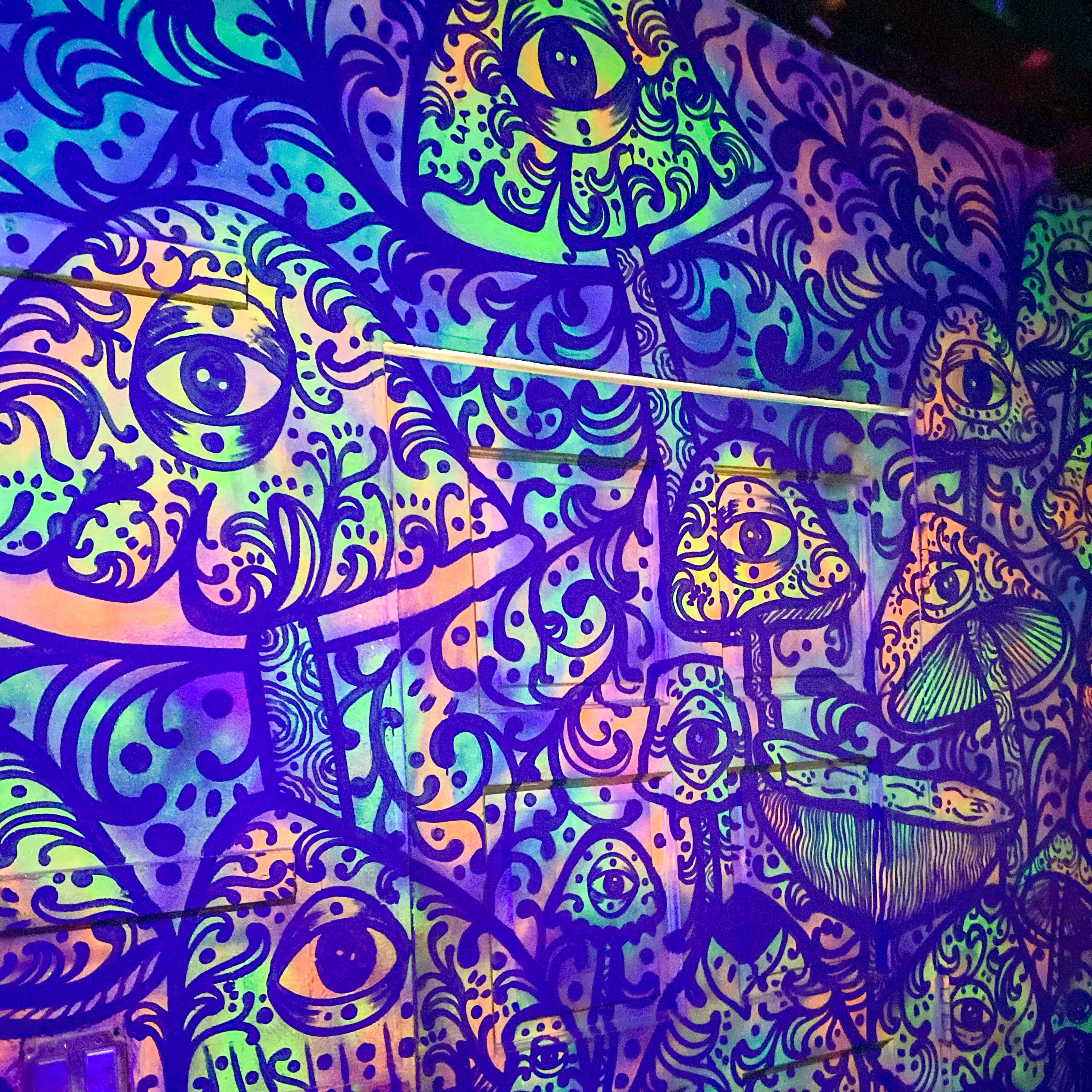 A colorful mural of mushrooms and eyes on a wall, illuminated with vibrant patterns.