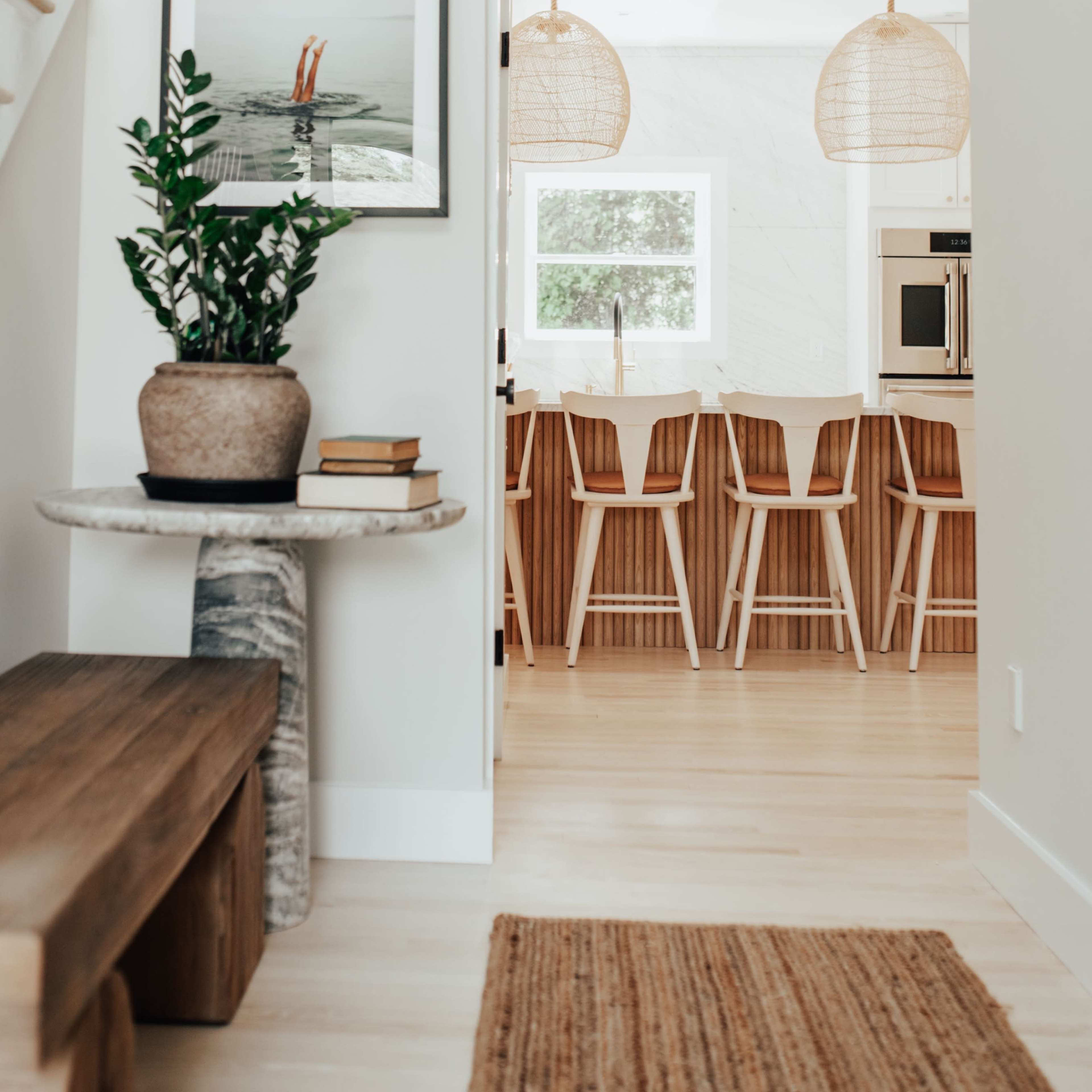A well-lit entryway leads to a modern kitchen with wooden bar stools and large woven pendant lights.