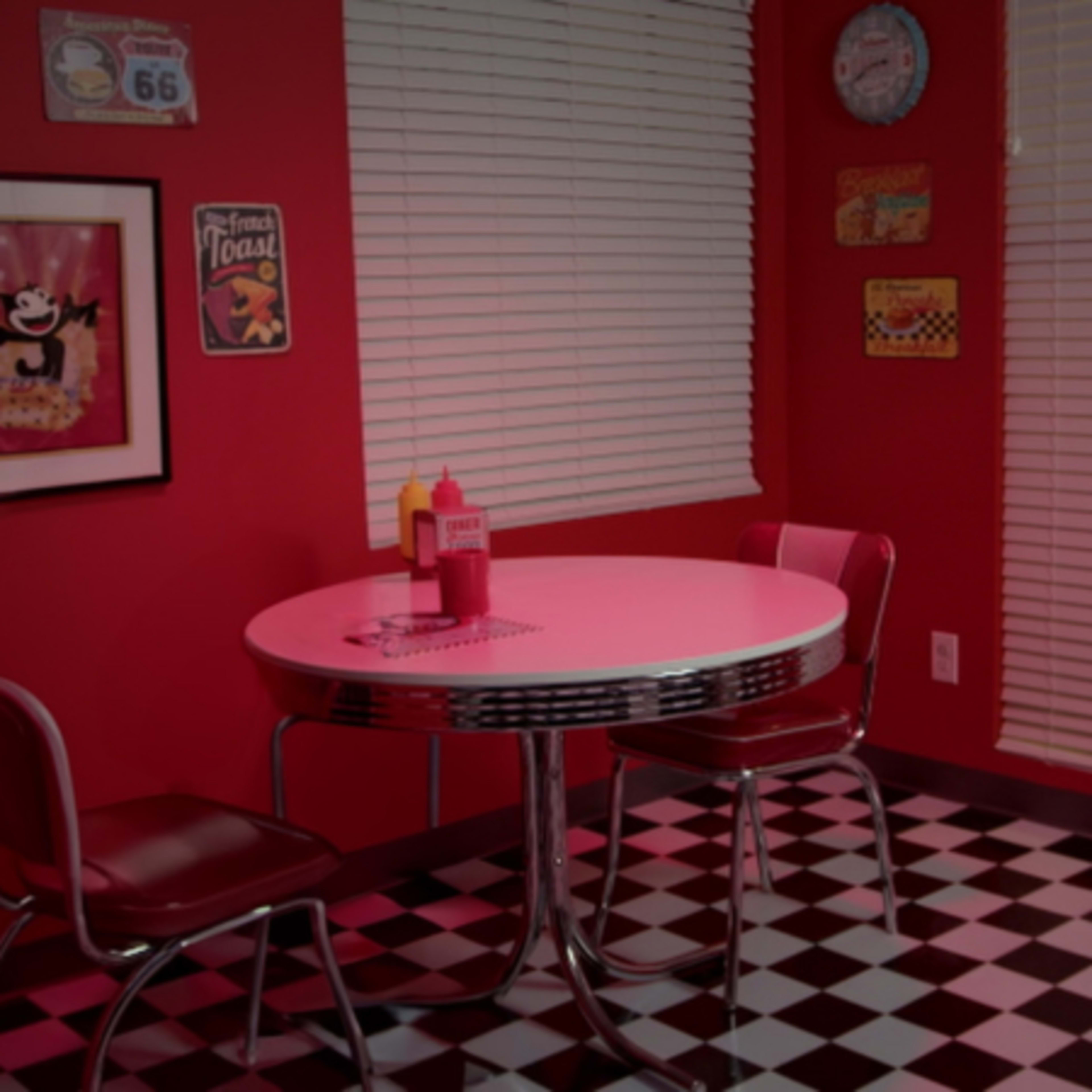 A retro diner-style kitchen features a round table with red chairs and black-and-white checkered flooring.