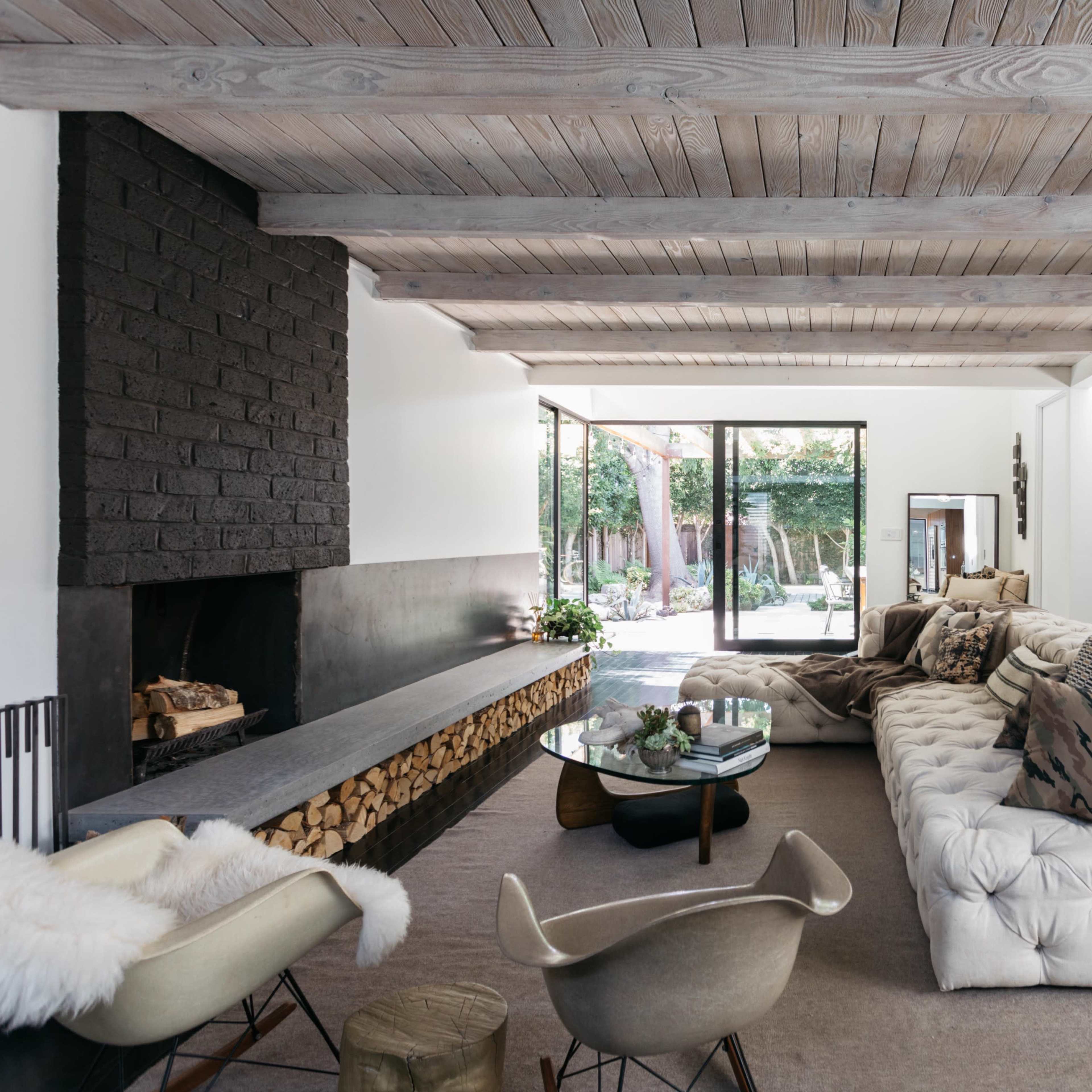 A modern living room with a tufted sofa, a large window overlooking a garden, and a minimalist fireplace.