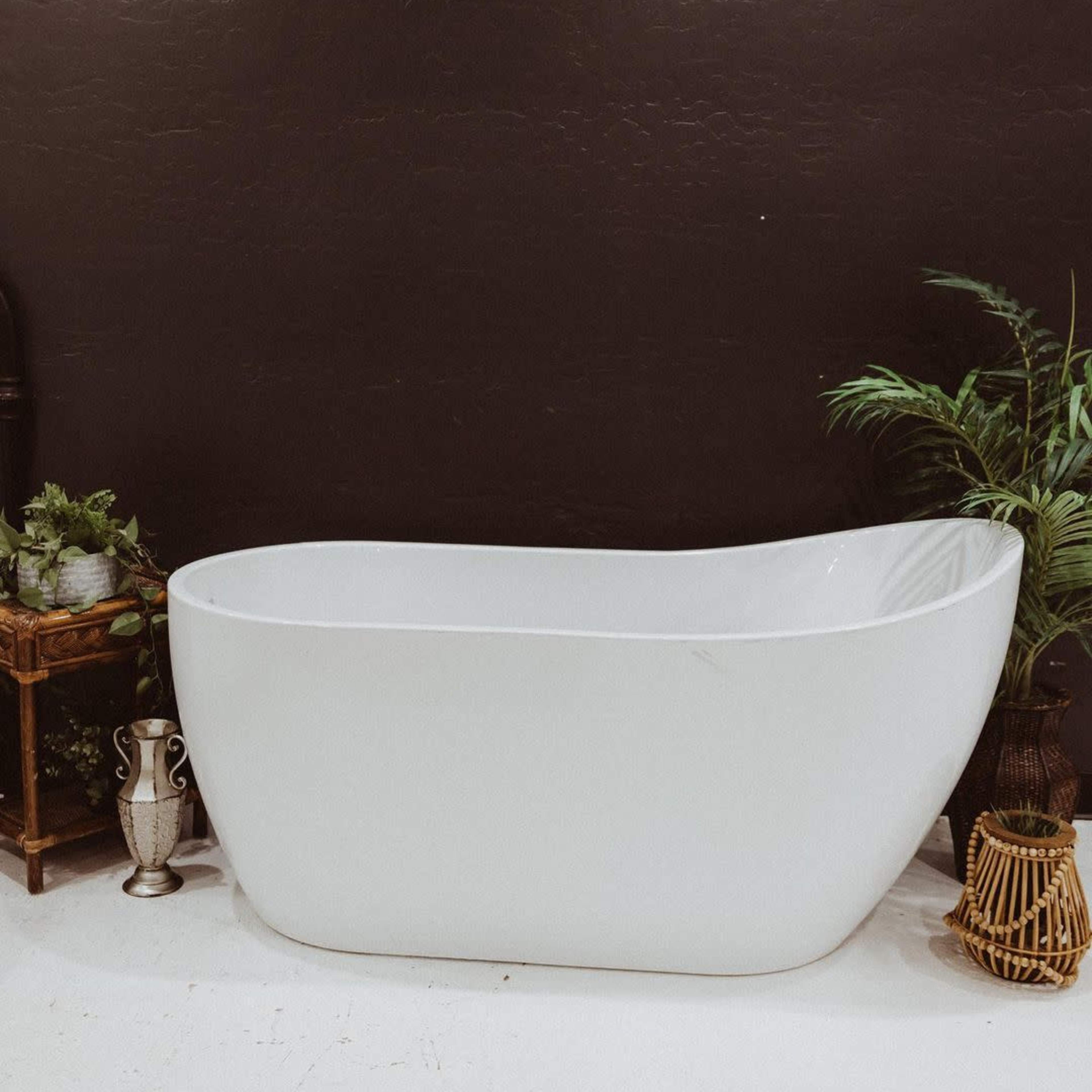 A modern white bathtub against a dark textured wall, surrounded by potted plants and decorative items.