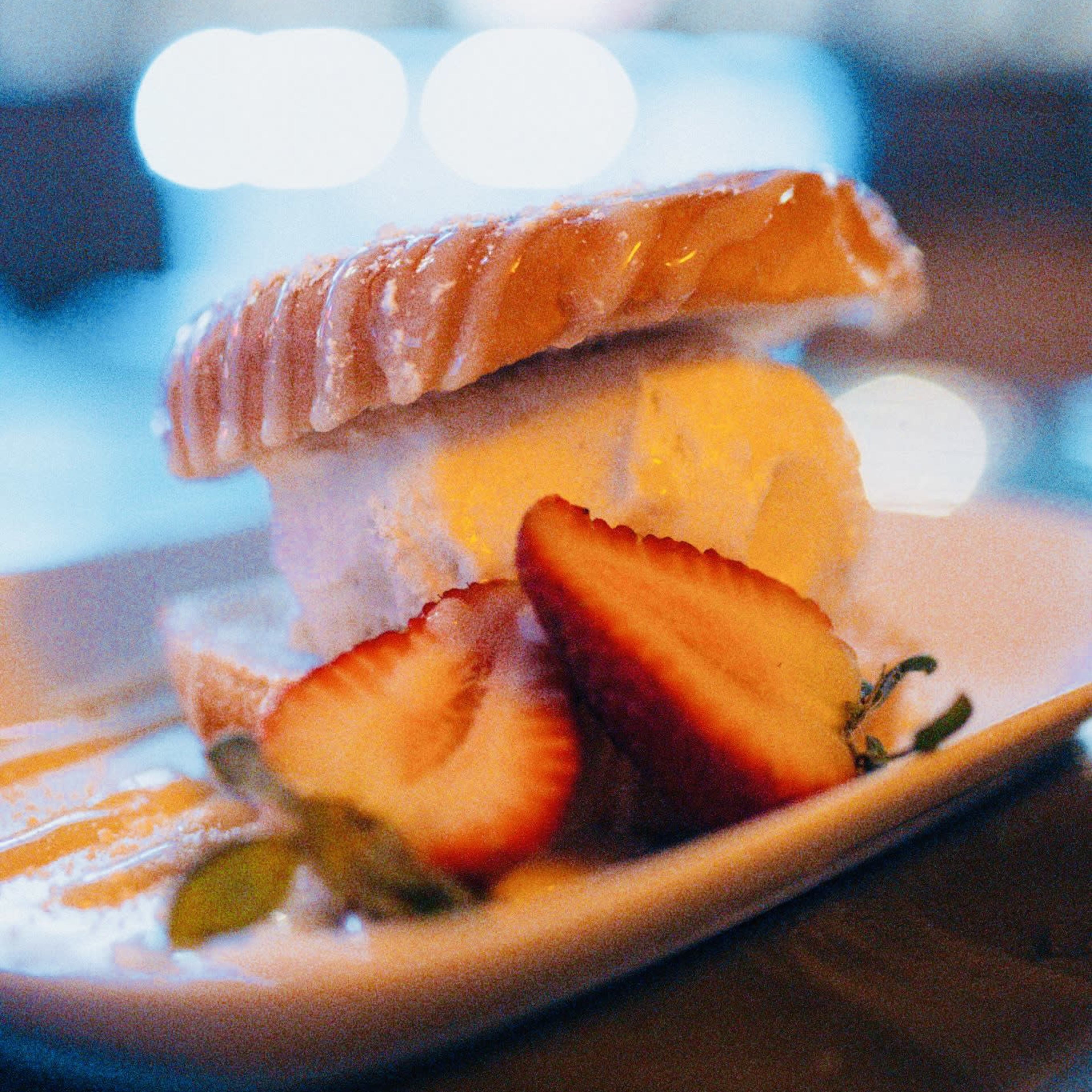 A dessert plate features a layer of cake and a scoop of ice cream, garnished with slices of fresh strawberries.