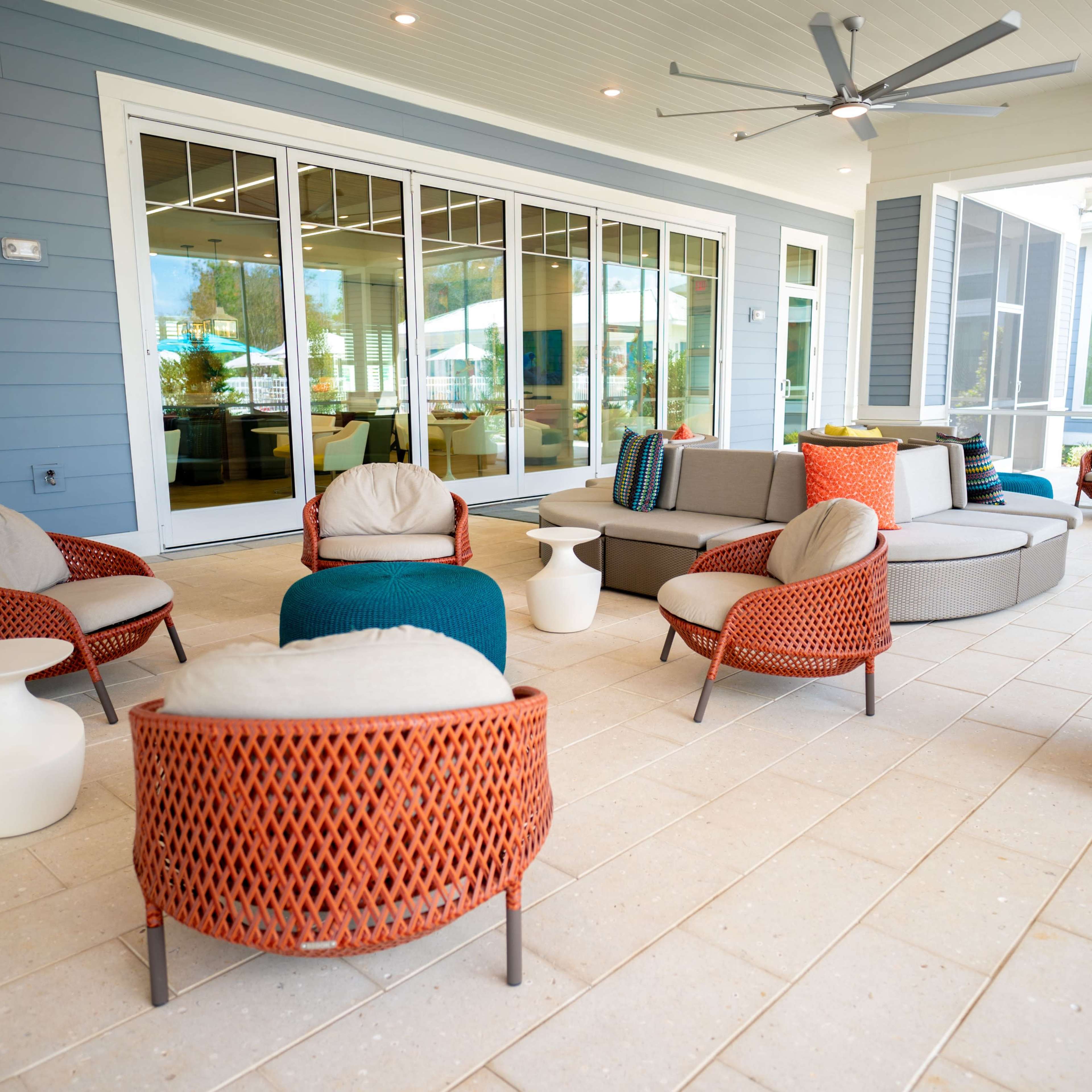 A modern outdoor seating area with several woven chairs, a circular table, and a large ceiling fan, all arranged on a tiled patio.