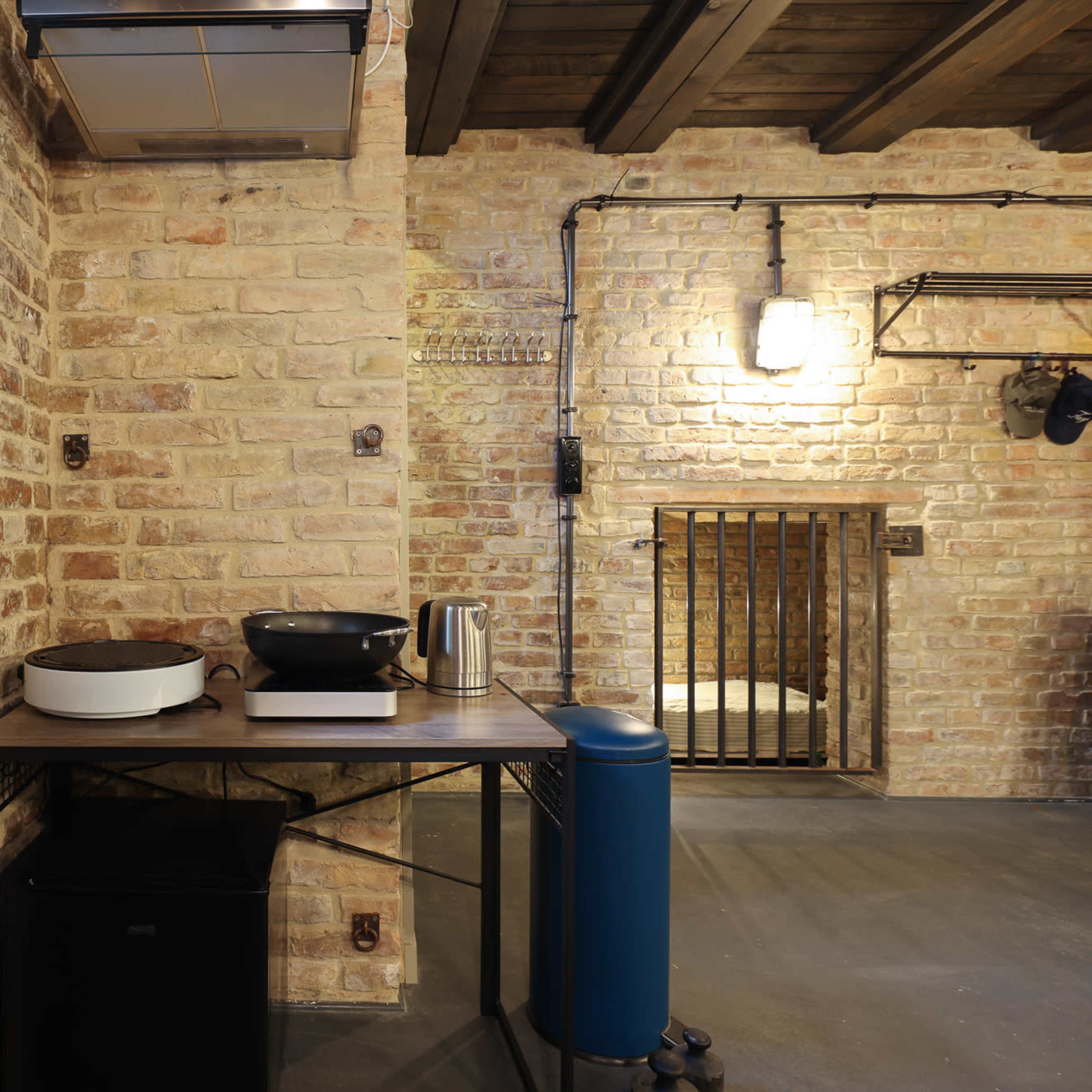 A modern kitchen area with exposed brick walls, a wooden shelf, and various kitchen appliances on a table.