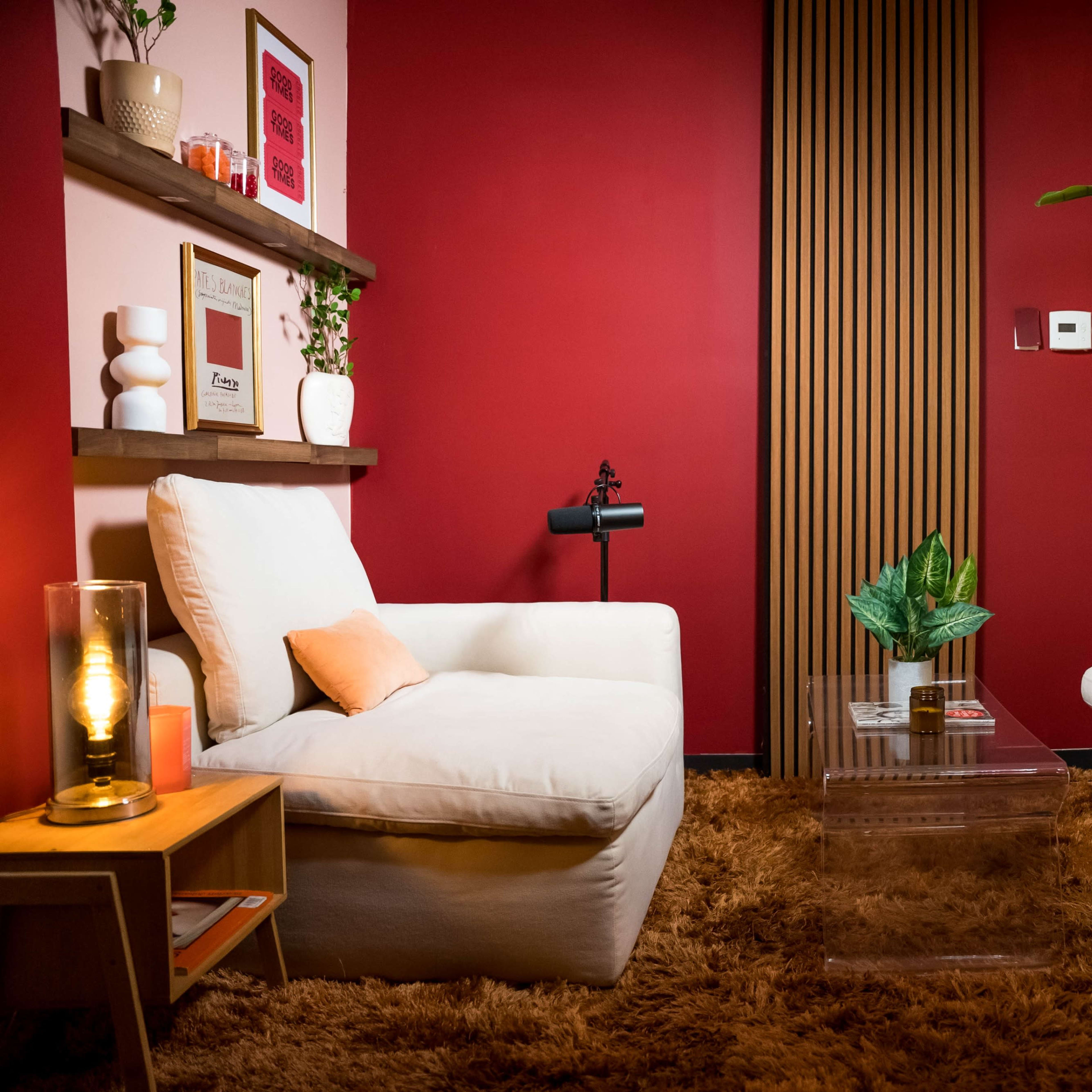 A cozy living room setup featuring two white armchairs, a small glass coffee table, a large potted plant, and a backdrop of a red wall with wooden paneling.
