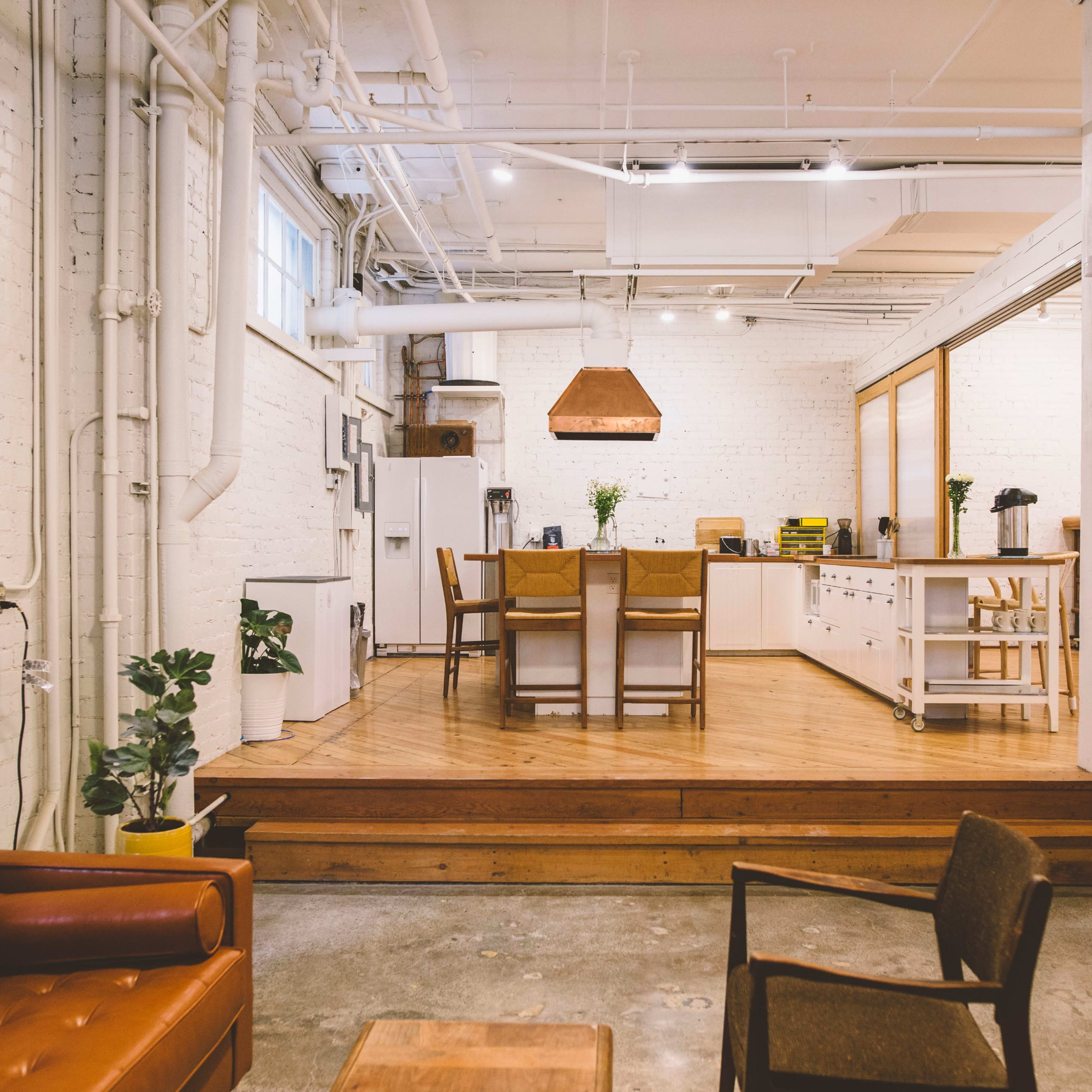 A spacious kitchen and dining area with wooden floors, modern furniture, and industrial-style lighting.