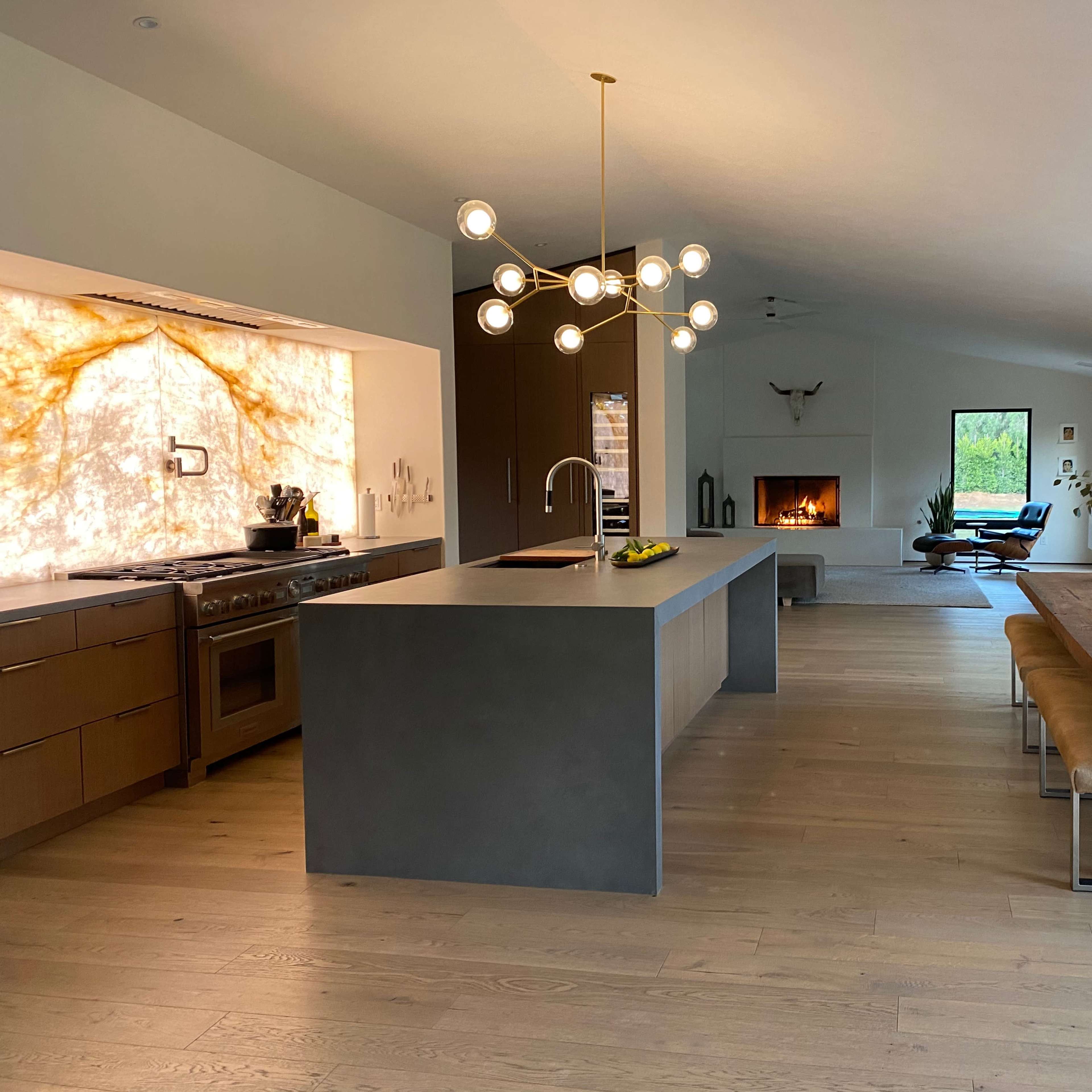 A modern kitchen with a large island and a stone feature wall, connected to a dining area and a living room featuring a fireplace and large windows.