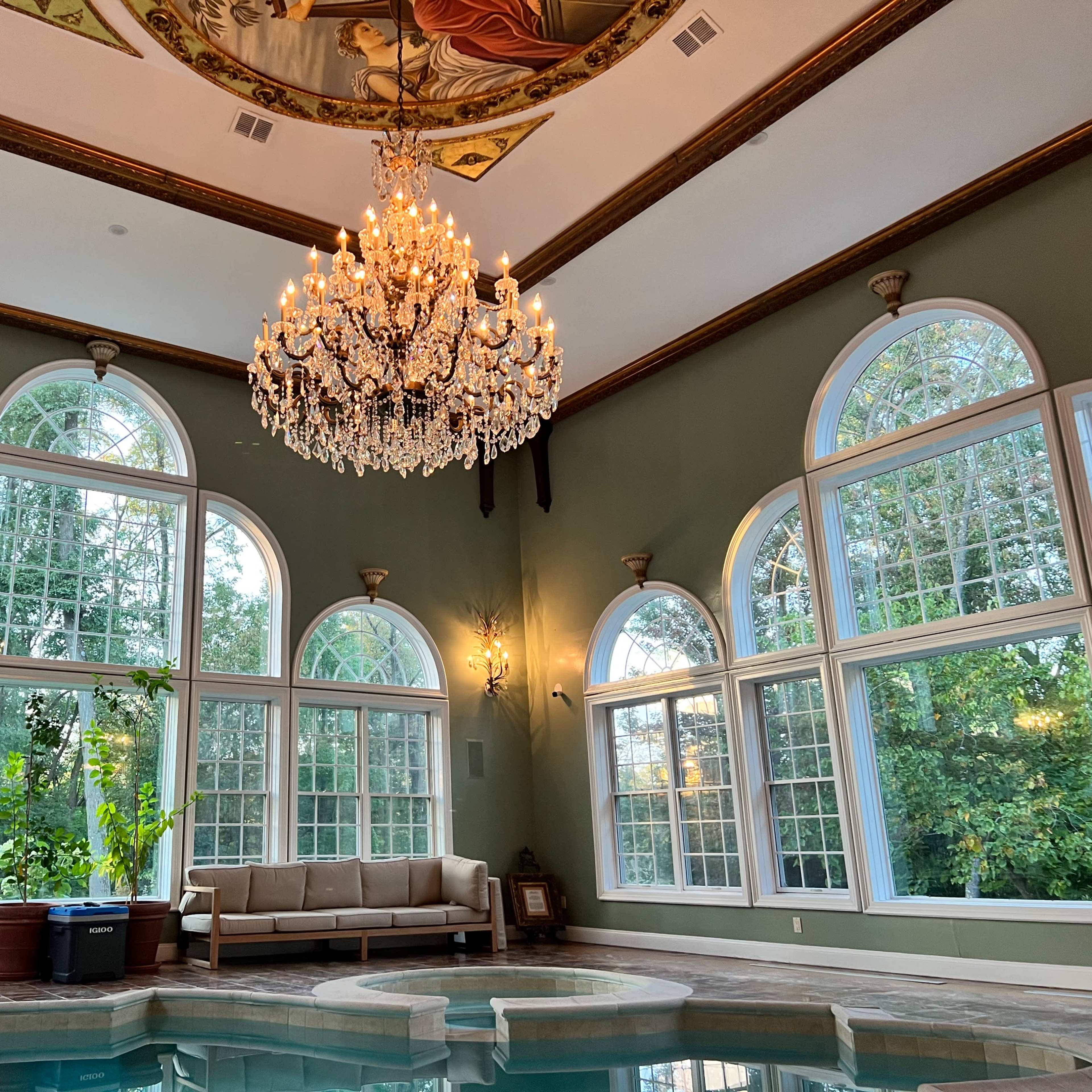 The scene features a well-lit indoor pool area with large arched windows, a chandelier, and a mural on the ceiling.