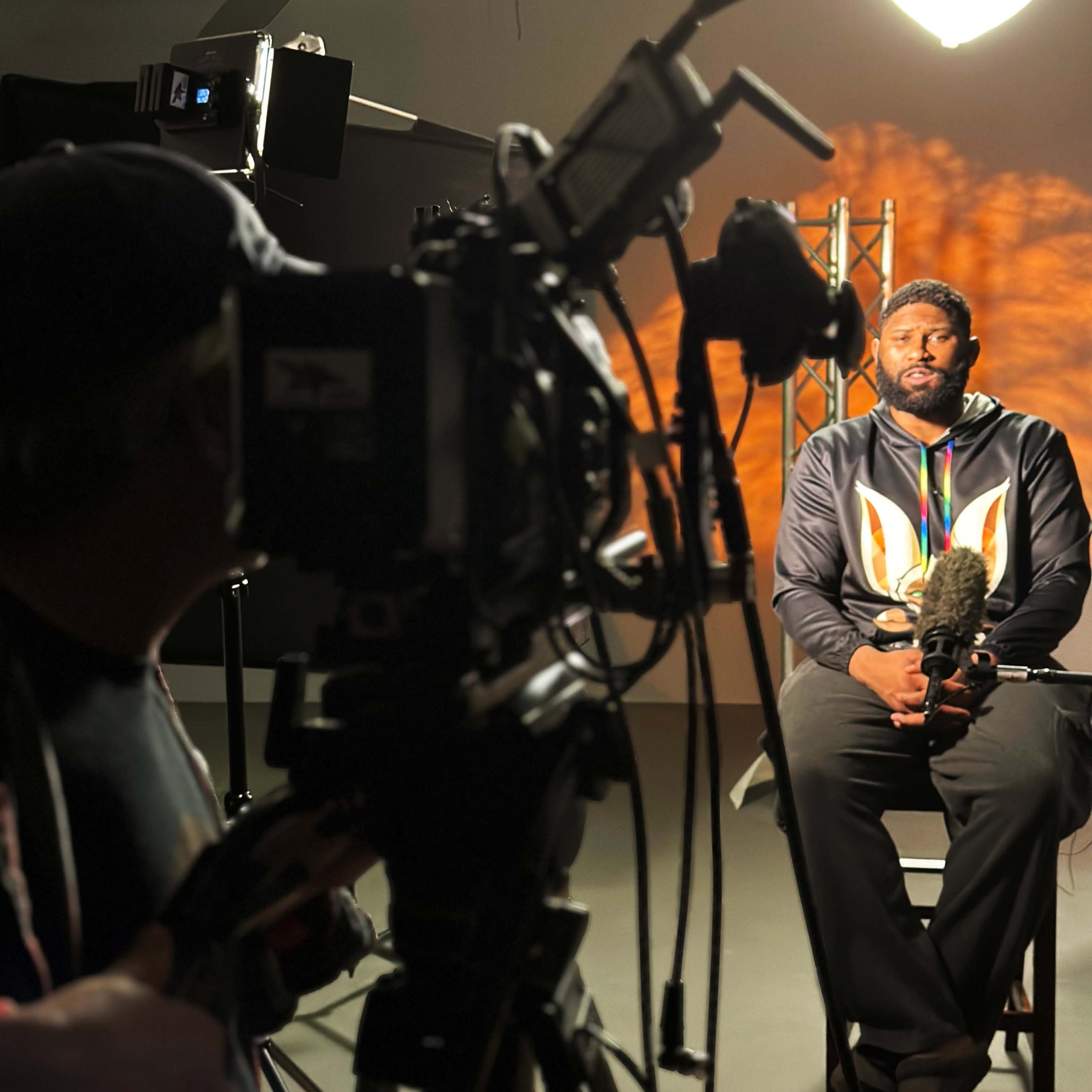A man sits in front of a camera and lighting setup during an interview.