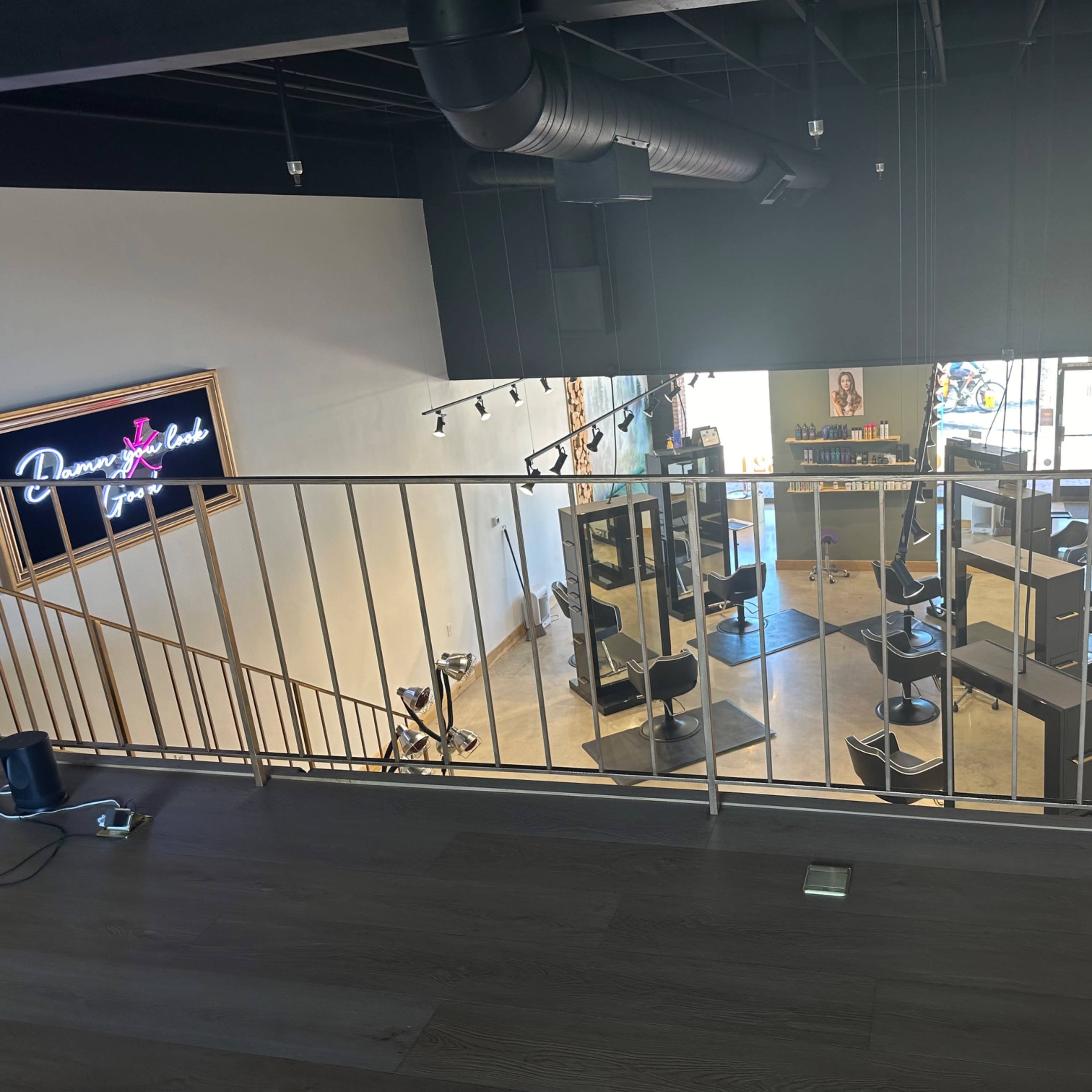 An elevated view of a hair salon featuring several styling stations, black chairs, and bright lighting.