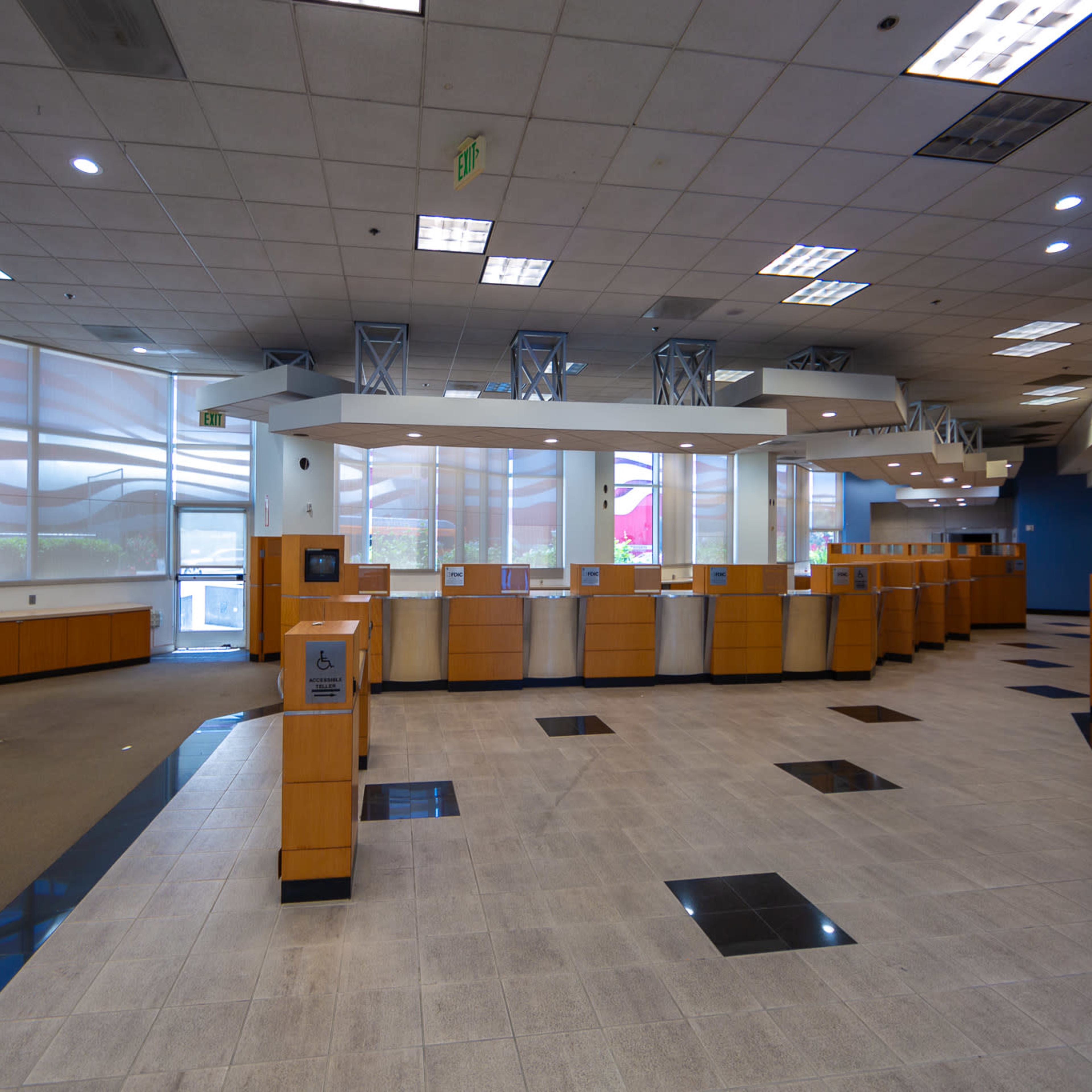 An empty bank interior with several teller stations and large windows allowing daylight to enter.