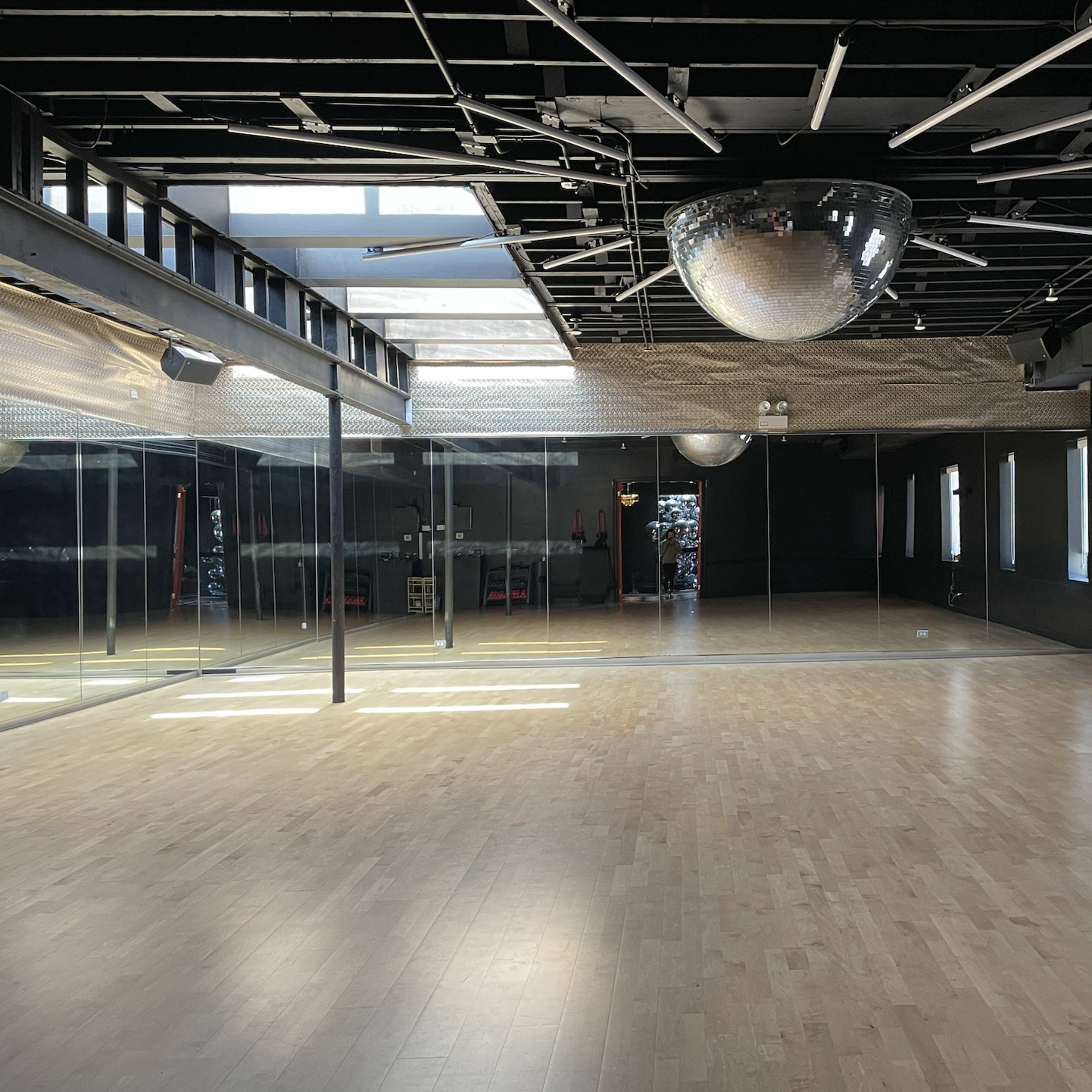 A spacious dance studio with wooden flooring, large mirrors on one wall, and a disco ball hanging from the ceiling.