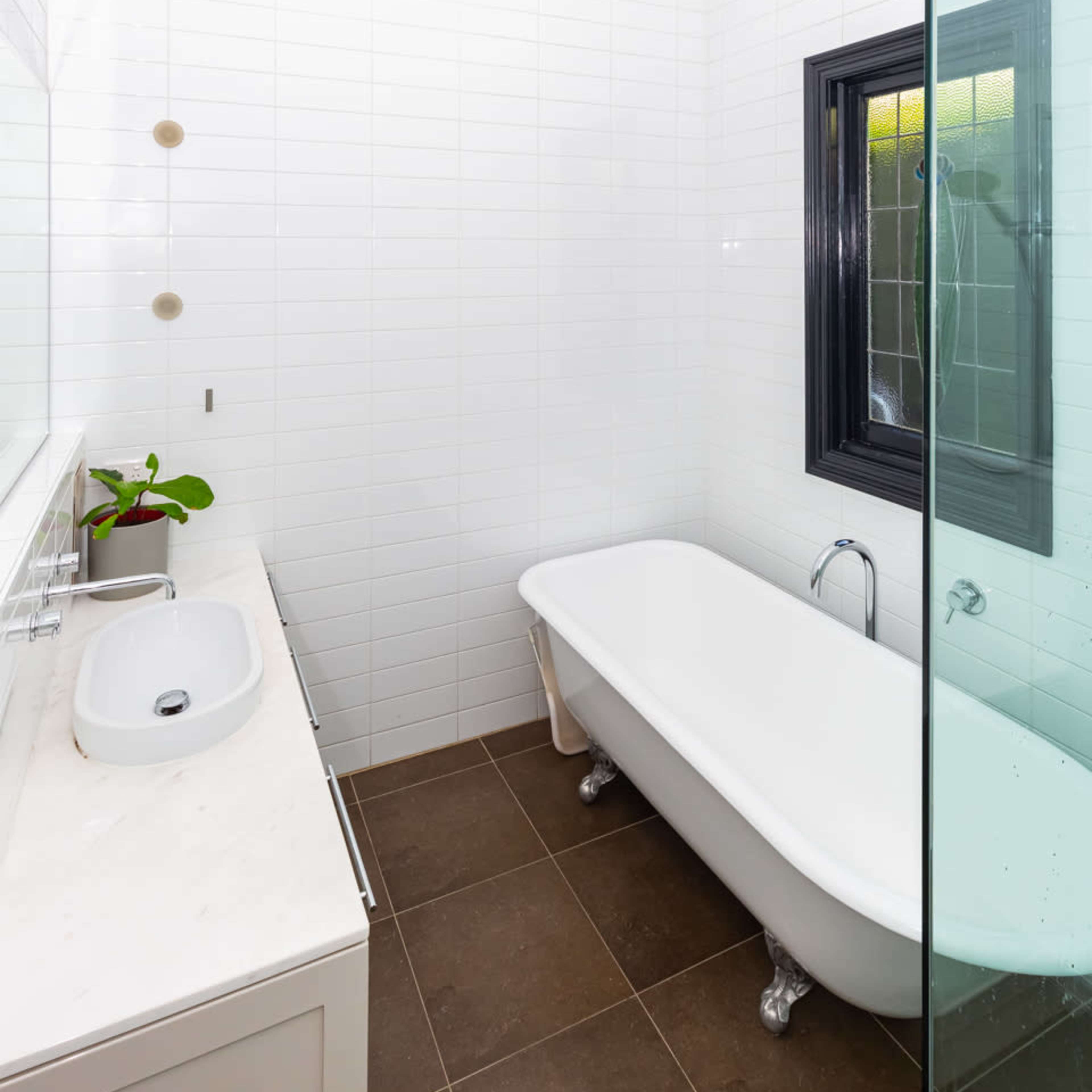 A modern bathroom featuring a freestanding white bathtub, a glass shower enclosure, a wall-mounted sink, and tiled walls in a light color.